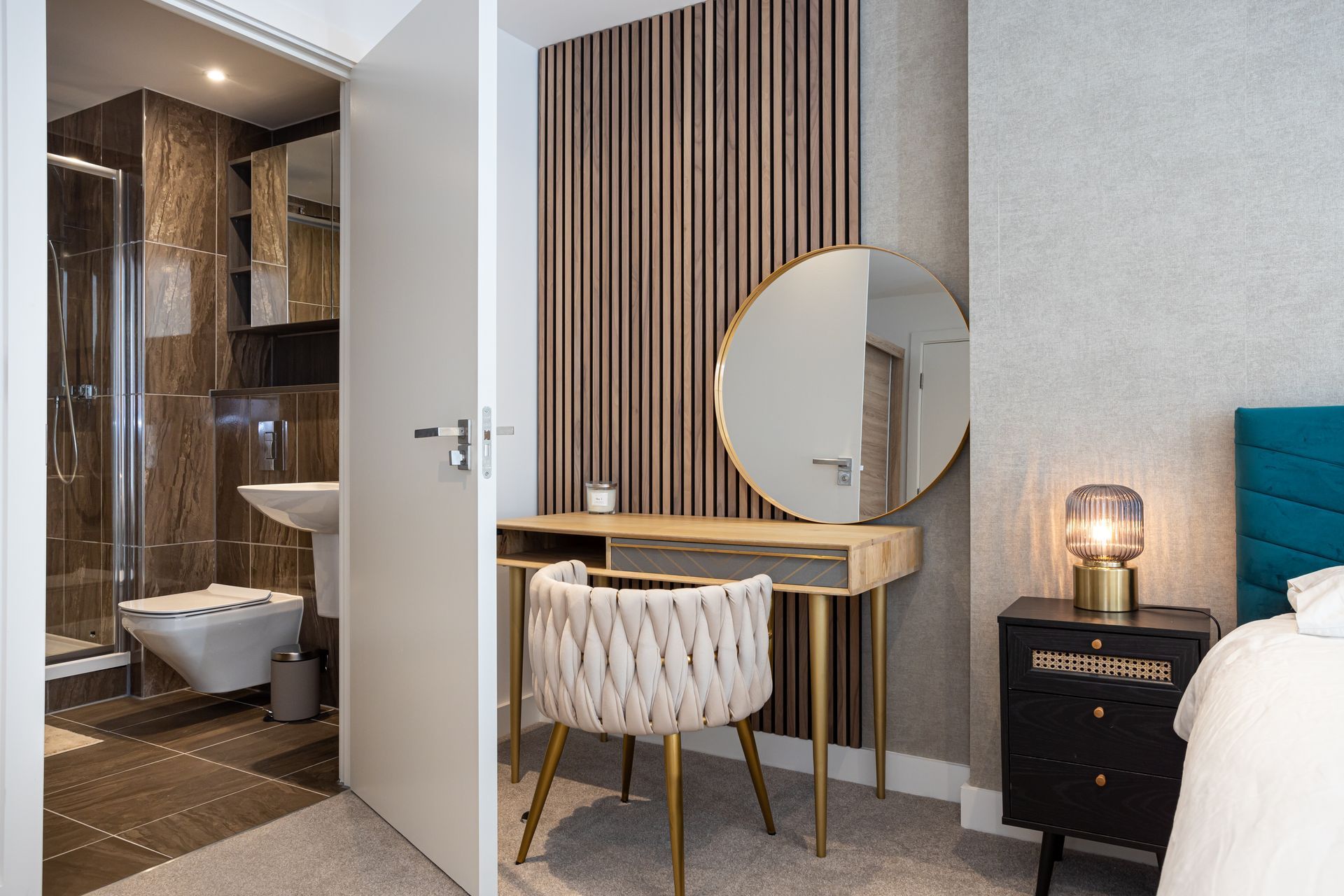 Bedroom with a vanity table, round mirror, and an adjacent bathroom with a toilet and sink.