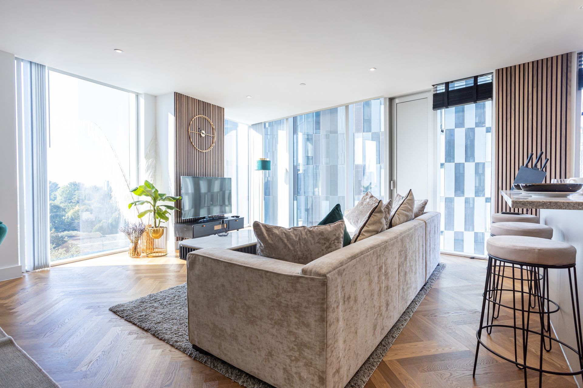 Modern living room with a large sofa, floor-to-ceiling windows, wooden floor, and a breakfast bar.