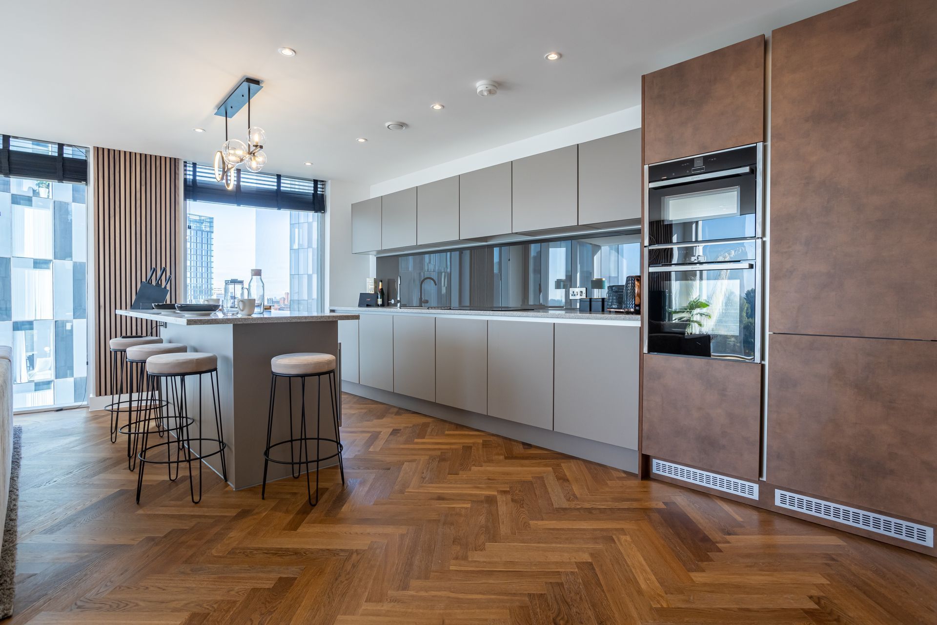 Modern kitchen with light wood herringbone floor, gray cabinets, and a brown appliance wall.
