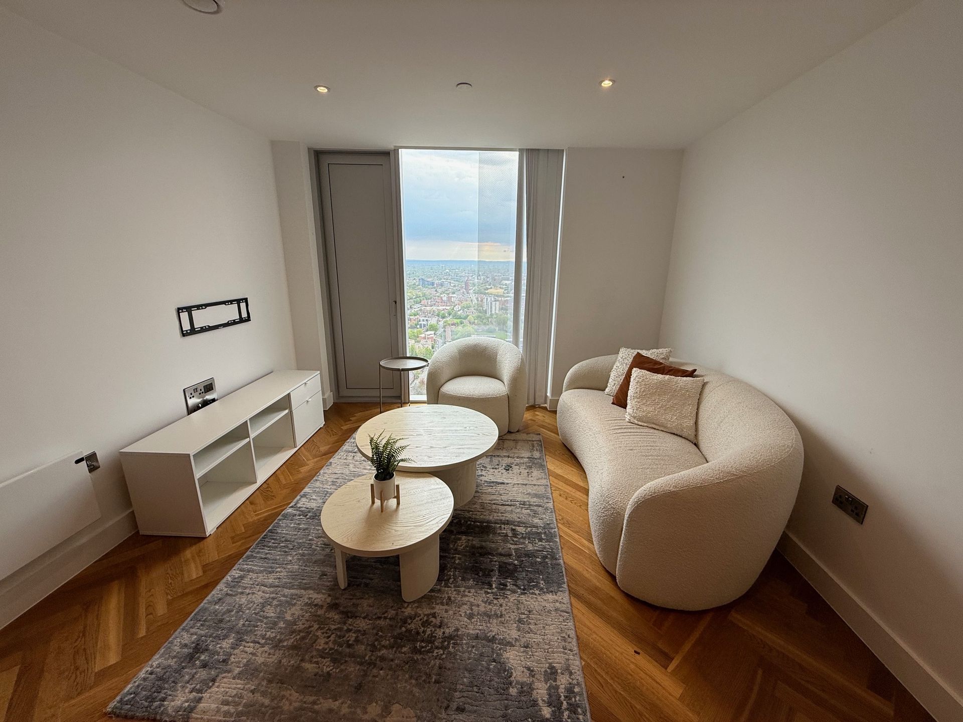 Modern living room with a curved sofa, rug, and city view through a large window.