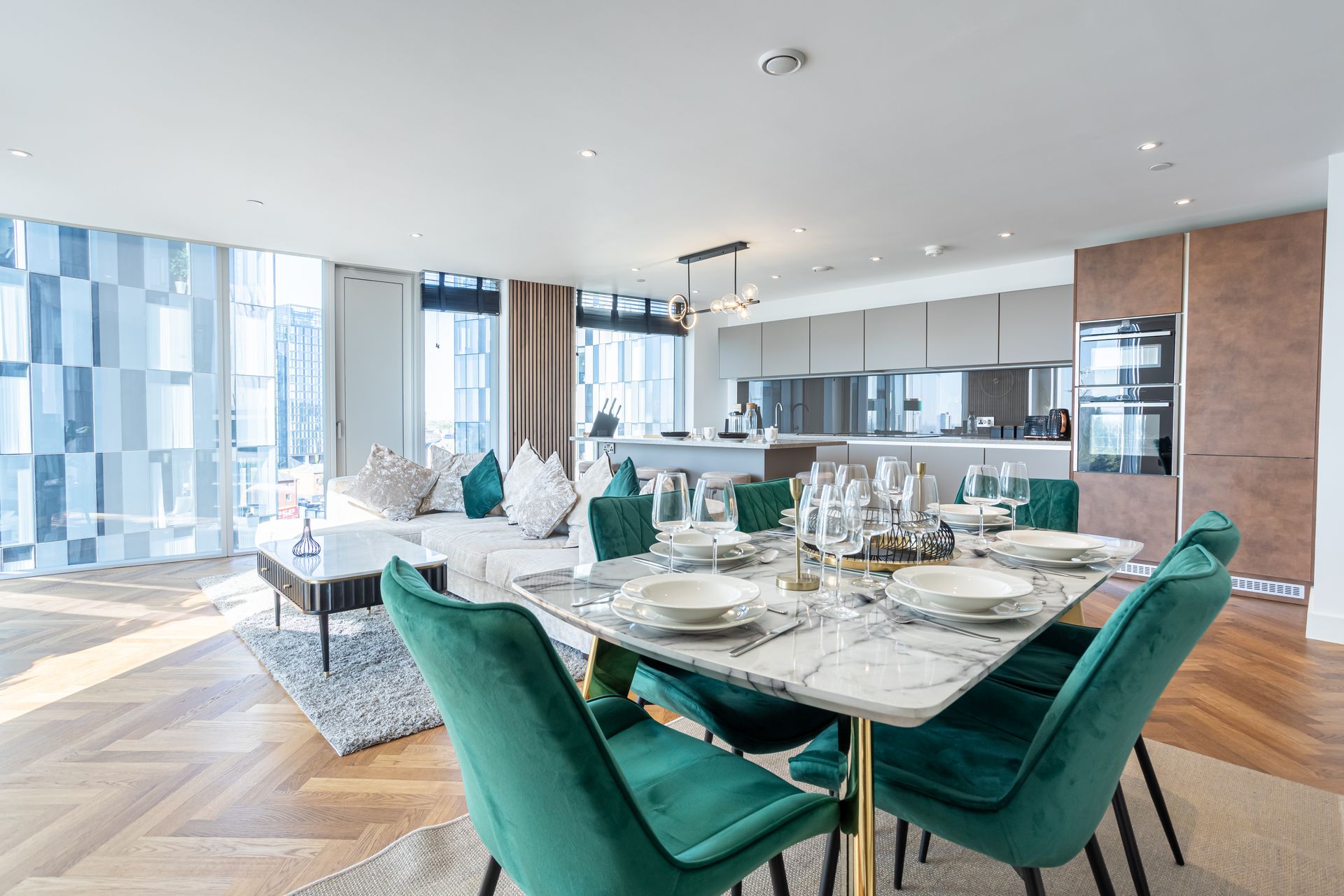 Luxurious open-plan living and dining area with marble table, emerald chairs, and white sofa near a window.