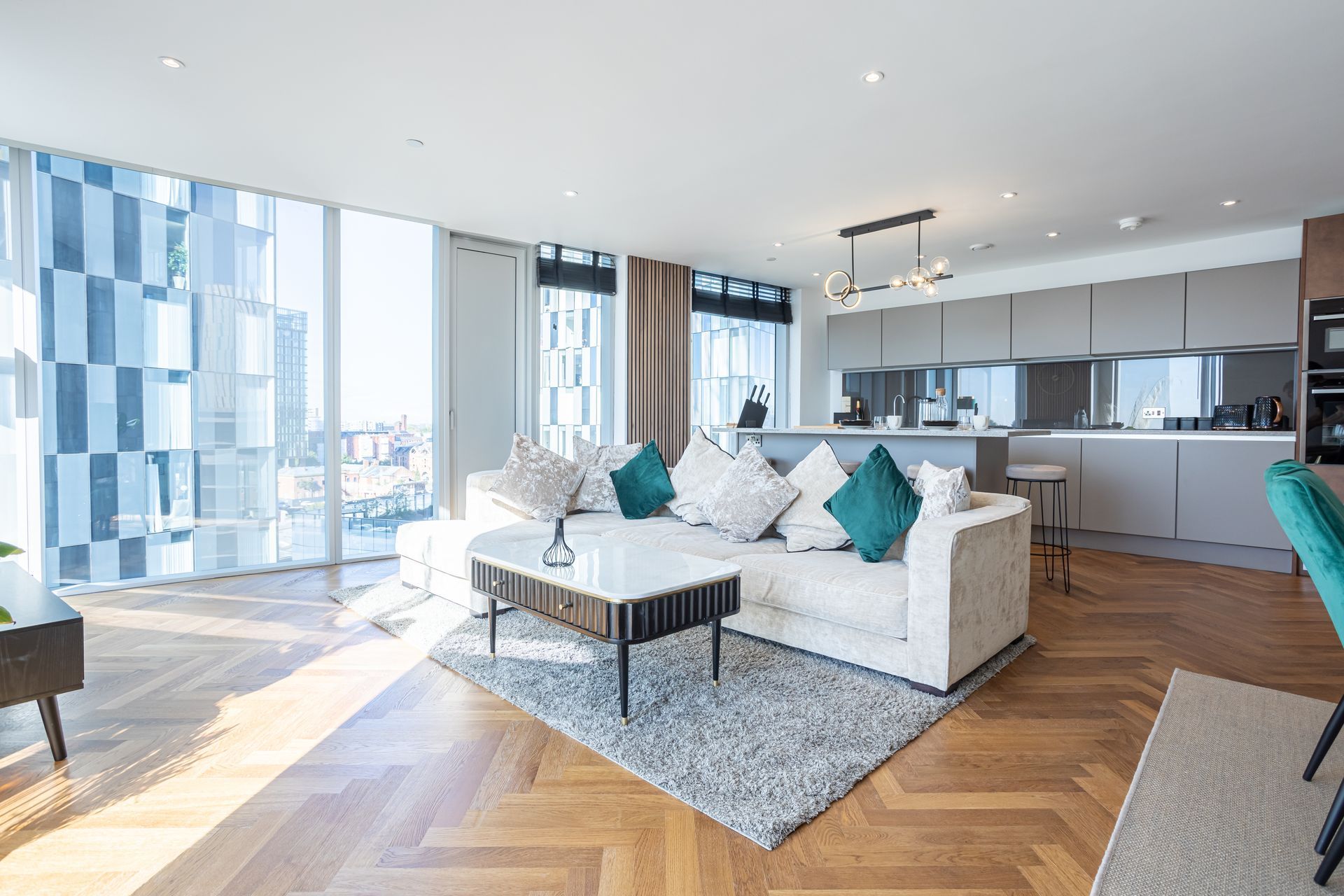 Modern apartment living room with white sofa, kitchen, and large windows.