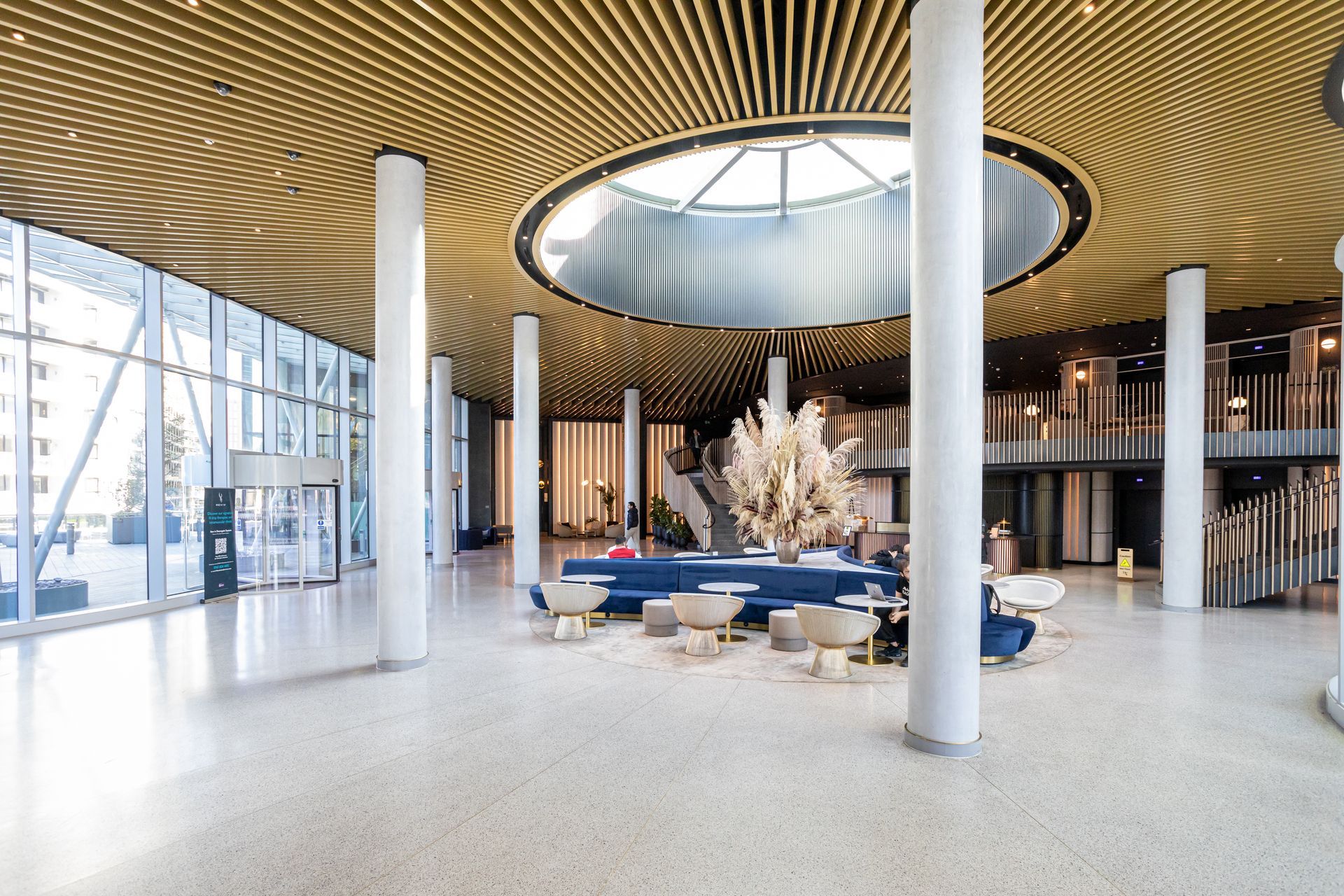 Spacious lobby with a circular skylight, white columns, blue sofa, and light-colored terrazzo floor.