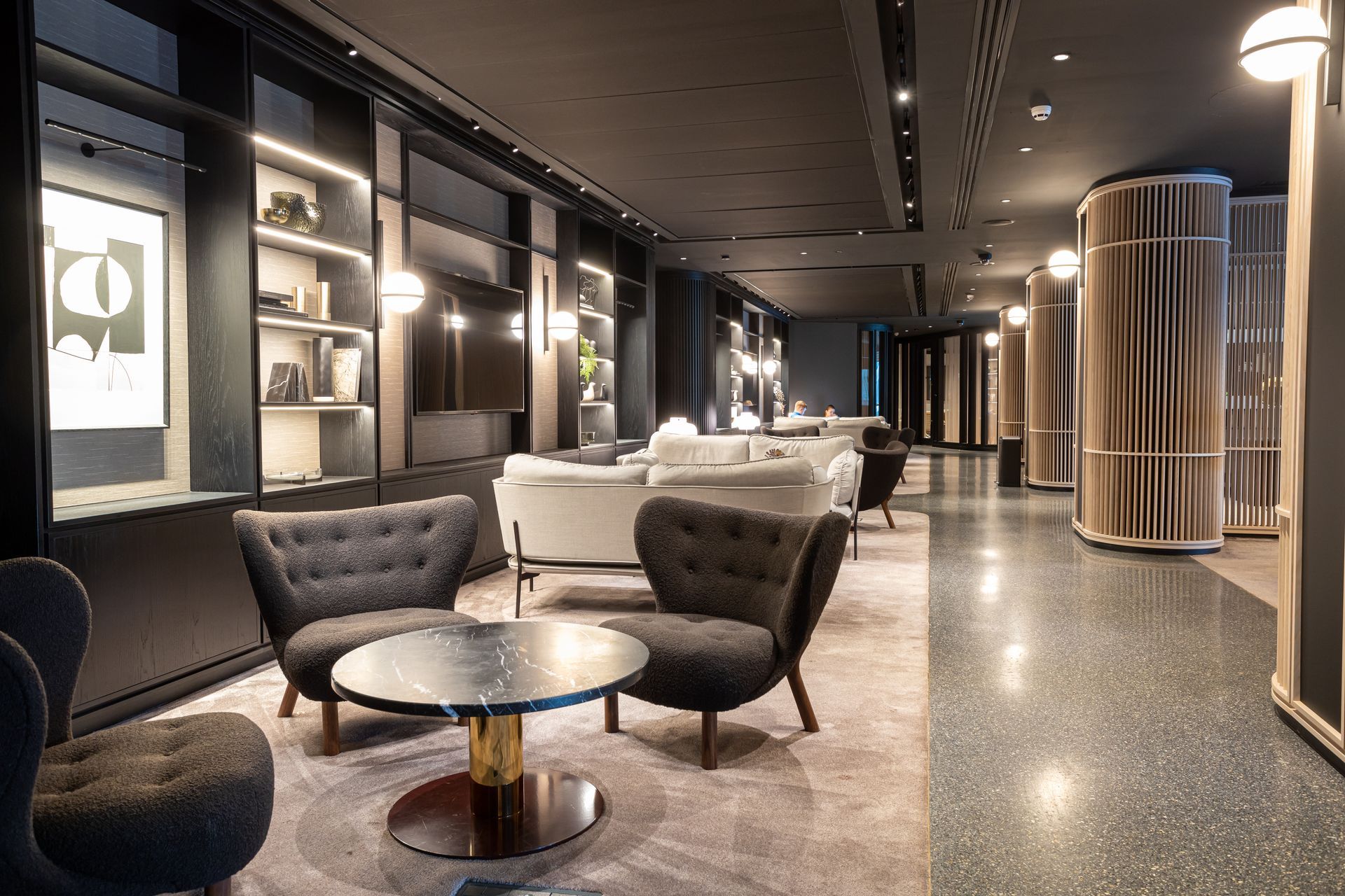 Elegant lounge with armchairs, a coffee table, built-in shelves, and decorative lamps. A hallway leads further into the room.