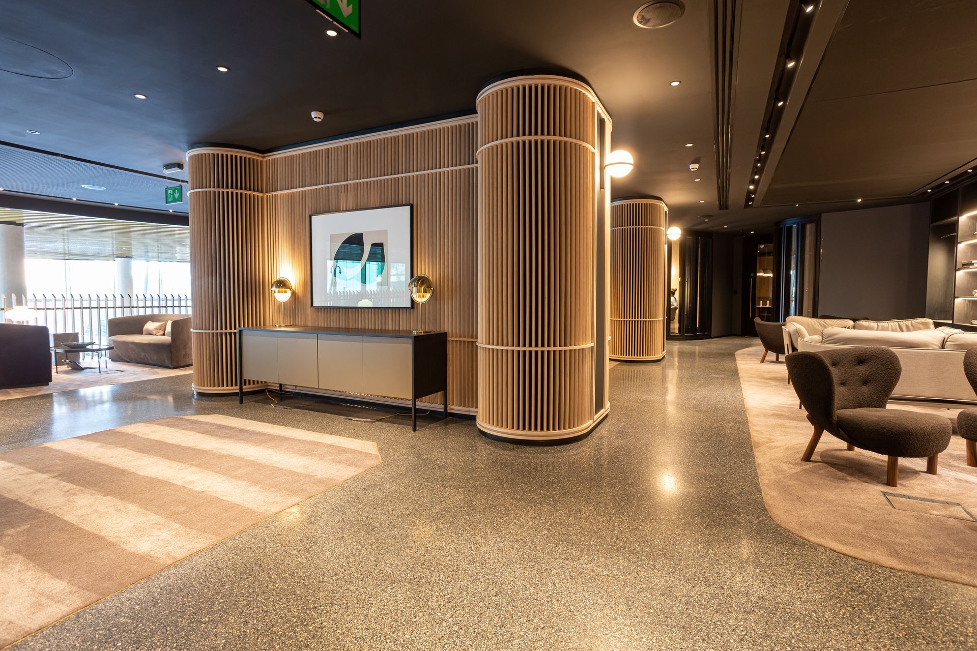 Lobby with light wood columns and accent walls. Terrazzo flooring with a light-colored rug and various seating areas.