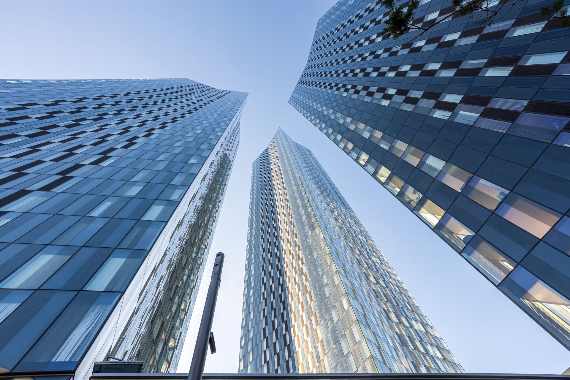 Three tall, modern glass skyscrapers reaching up toward a blue sky.