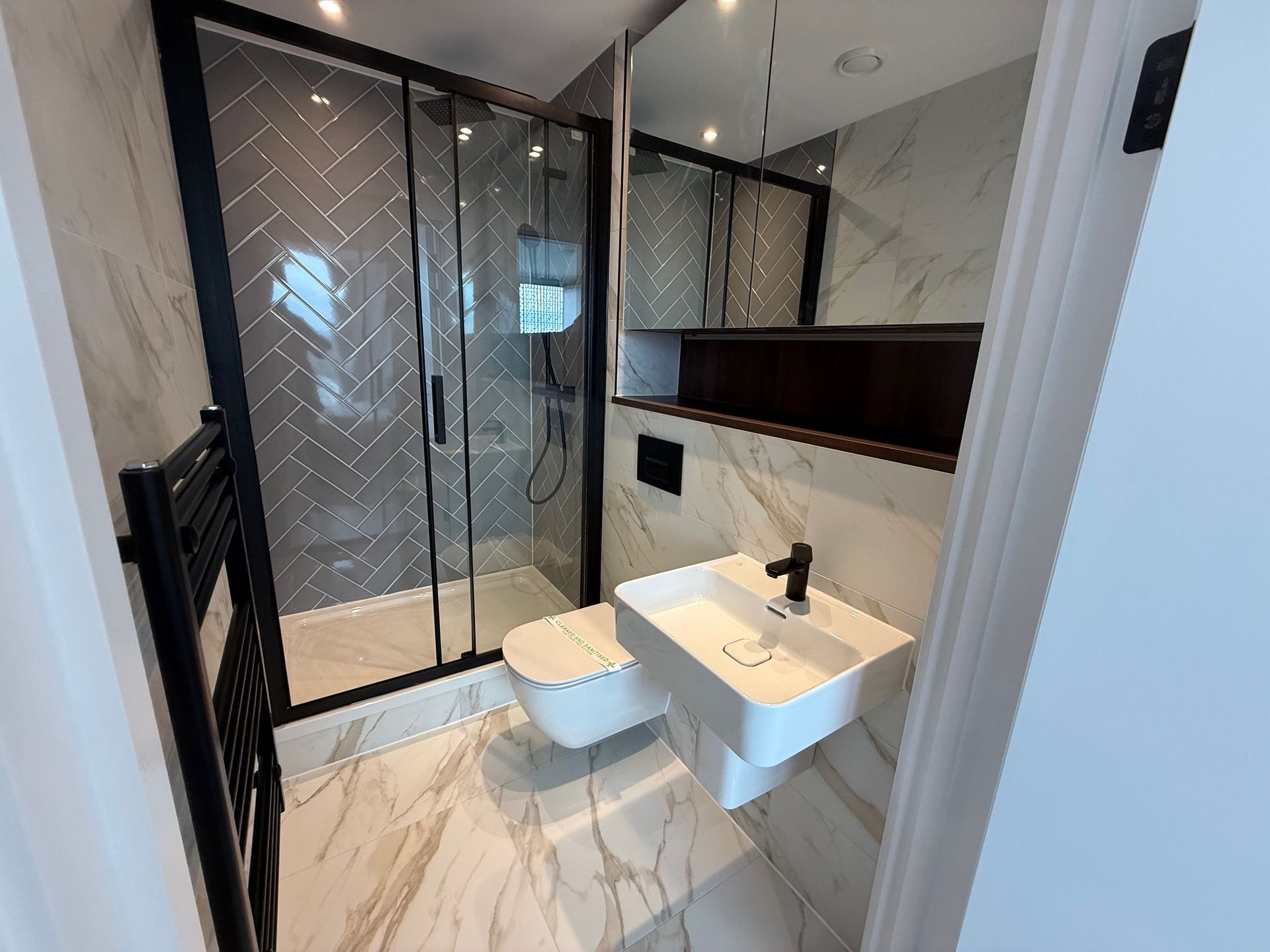 Modern bathroom with glass shower, floating sink, and marble-look tile.