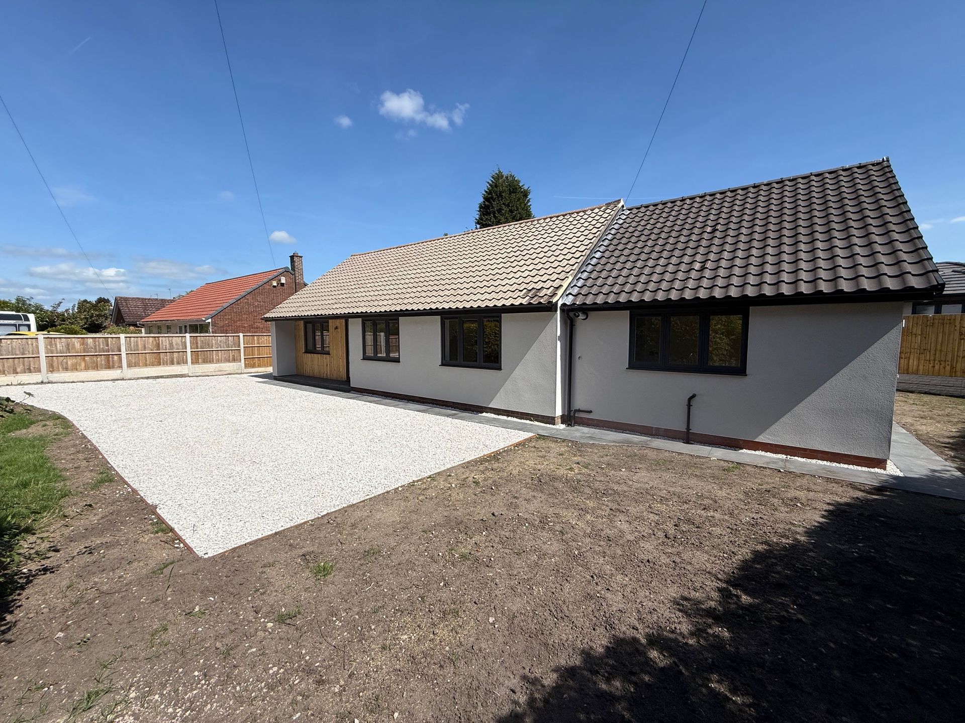 Bungalow undergoing roof renovation with gravel drive and unfinished yard against a blue sky.