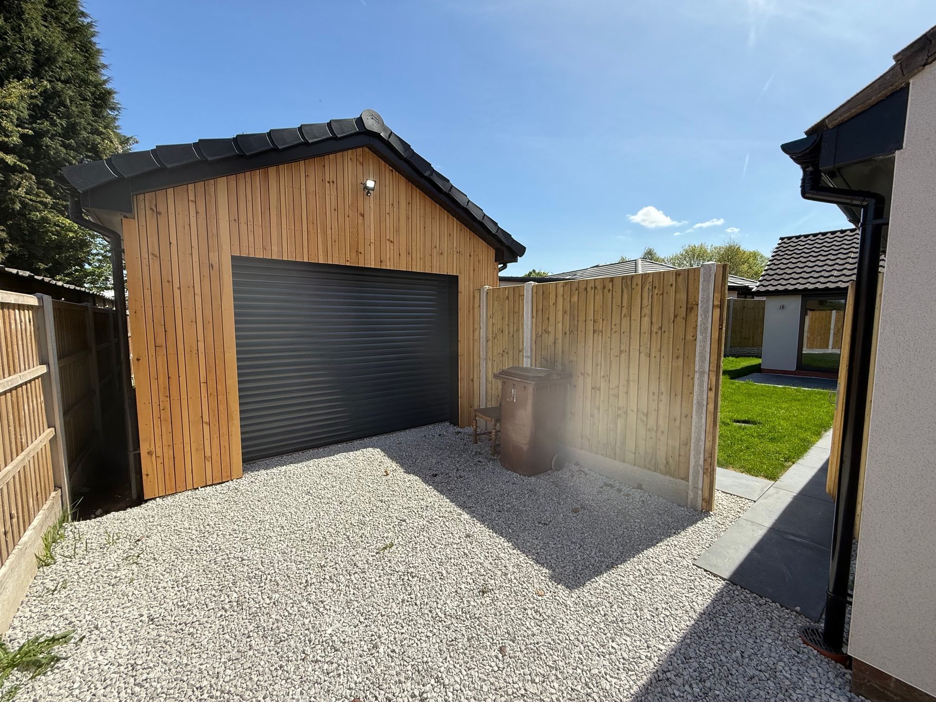 Garage with wooden siding and black door, gravel driveway.
