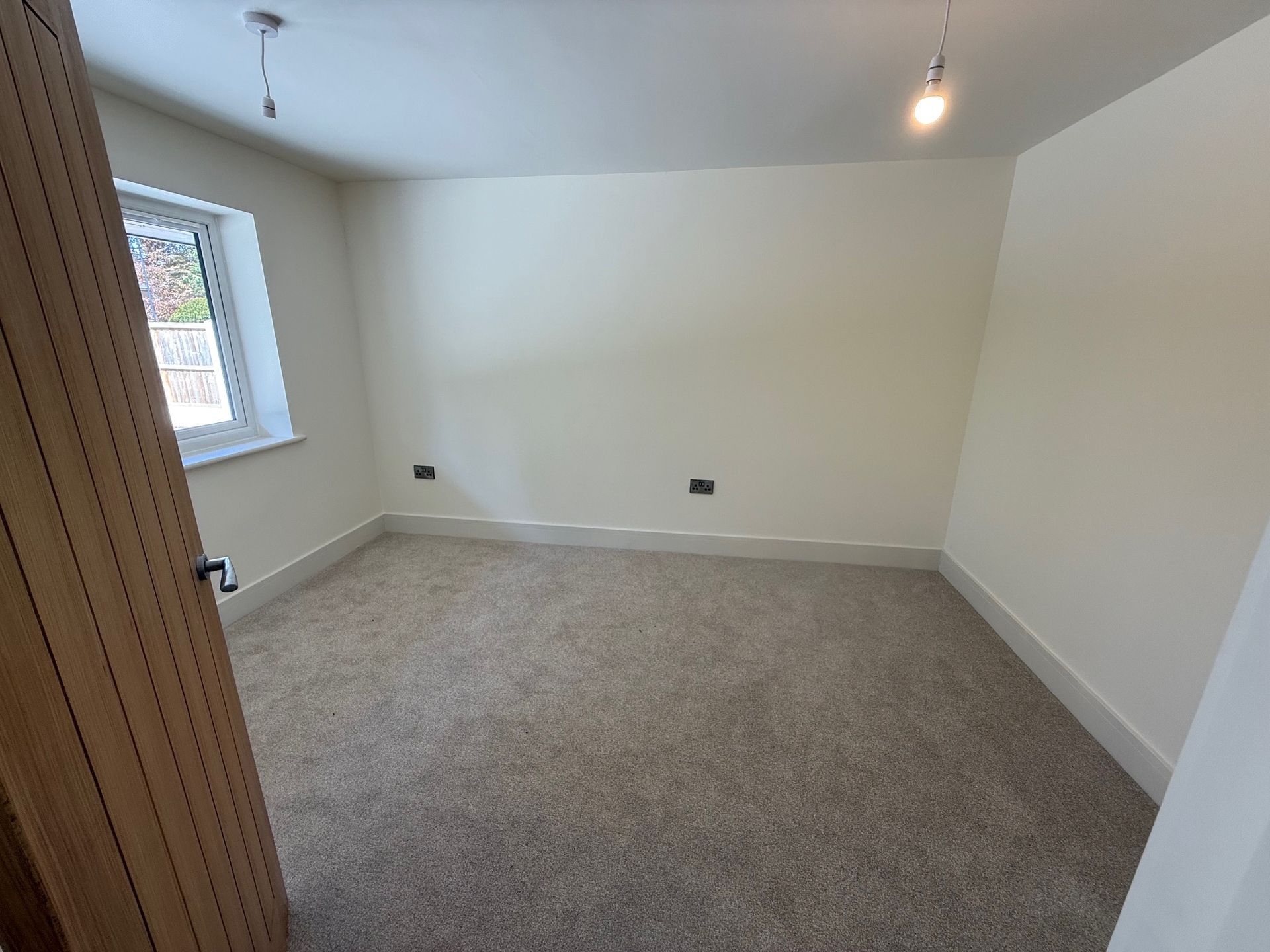 Empty room with light-colored walls, carpet, and a window. A door is ajar.