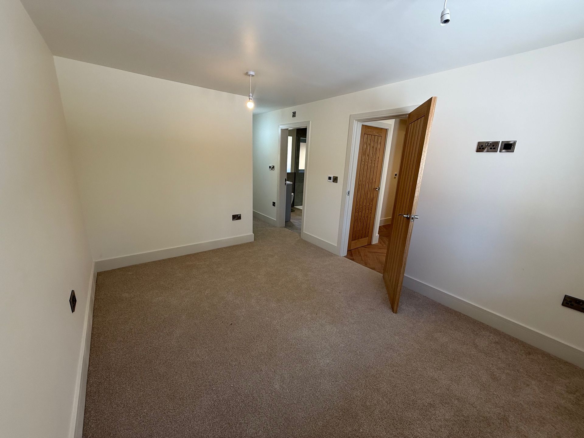 Empty room with beige carpet, white walls, and open wooden door to hallway.
