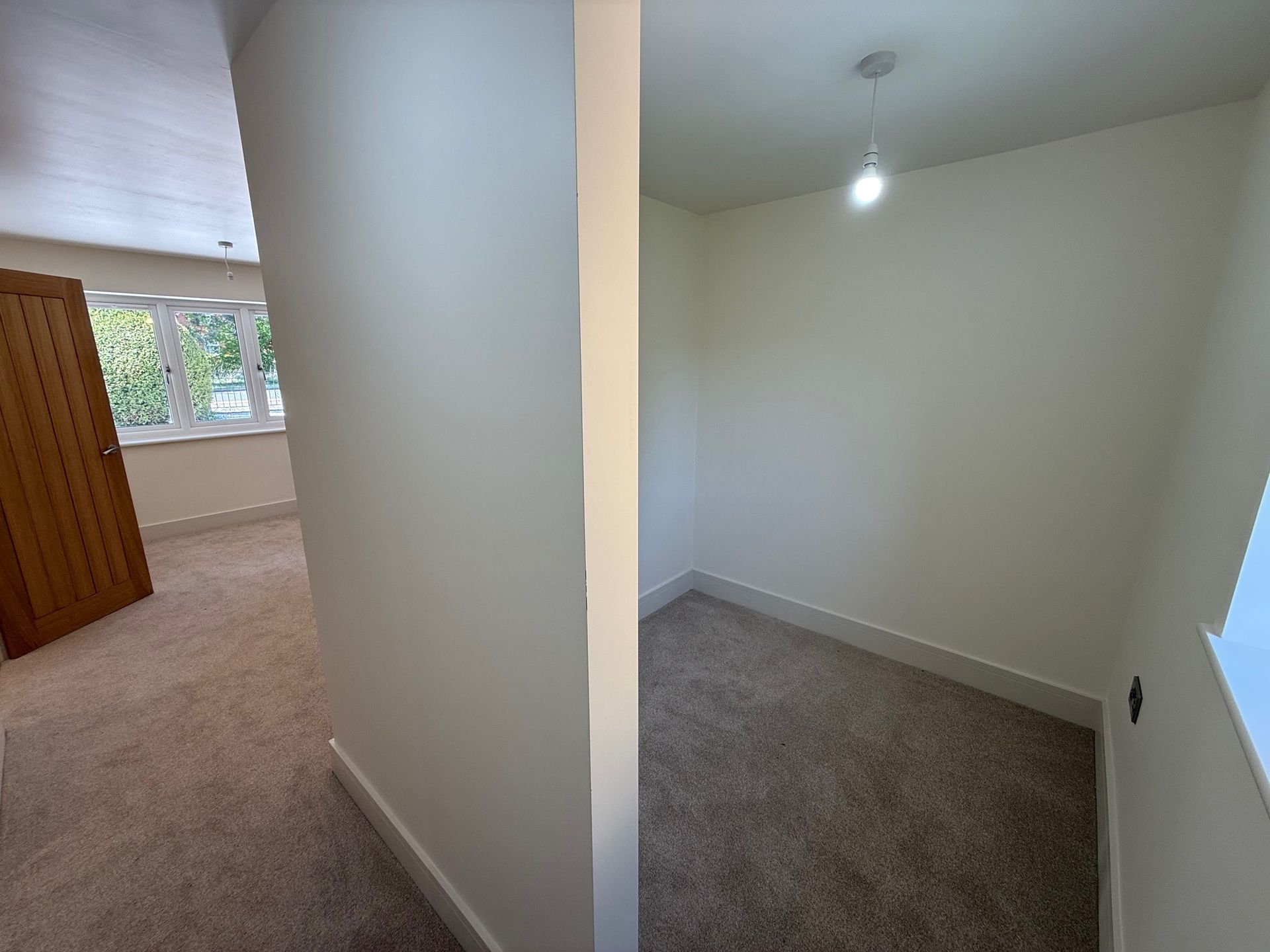Interior view: hallway with carpet, adjacent small room with a lightbulb, and a partially visible bedroom.