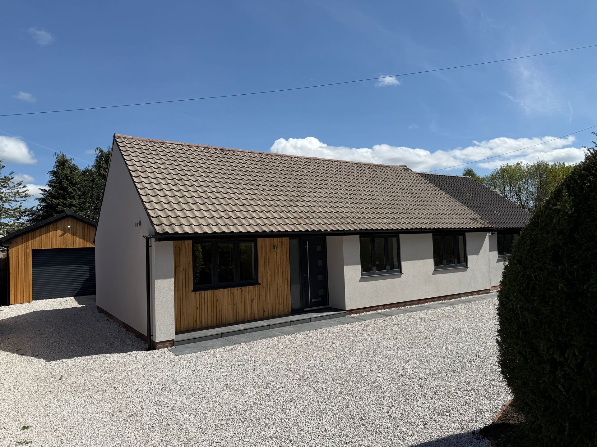 Bungalow with light gravel driveway and garage, beige walls, brown roof tiles, and wood accents.