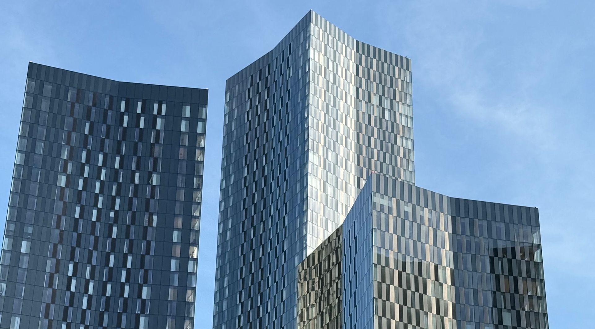 Three modern, tall, gray skyscrapers against a clear blue sky.