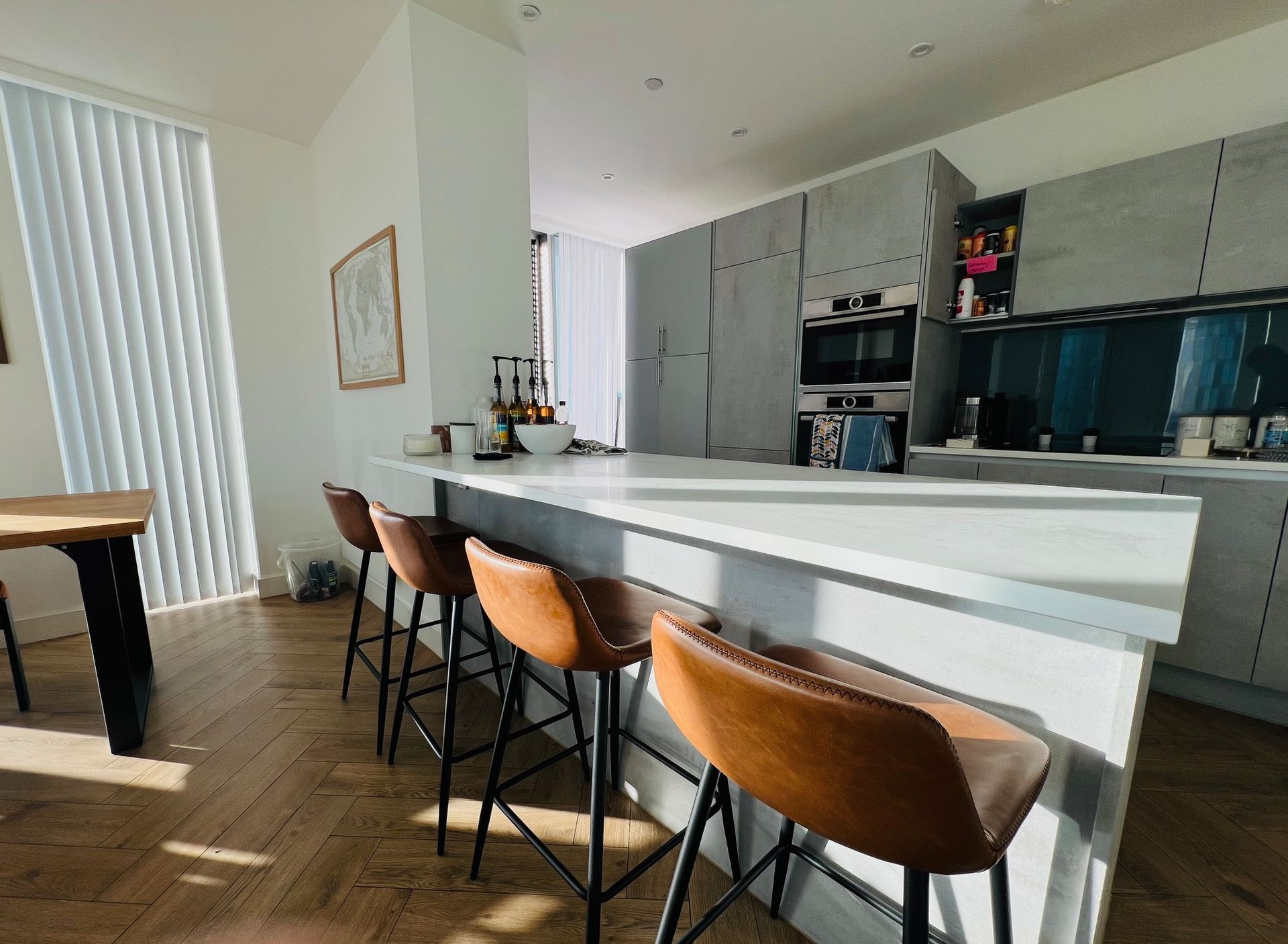 Modern kitchen with island, brown leather bar stools, light-colored countertops, and gray cabinetry.