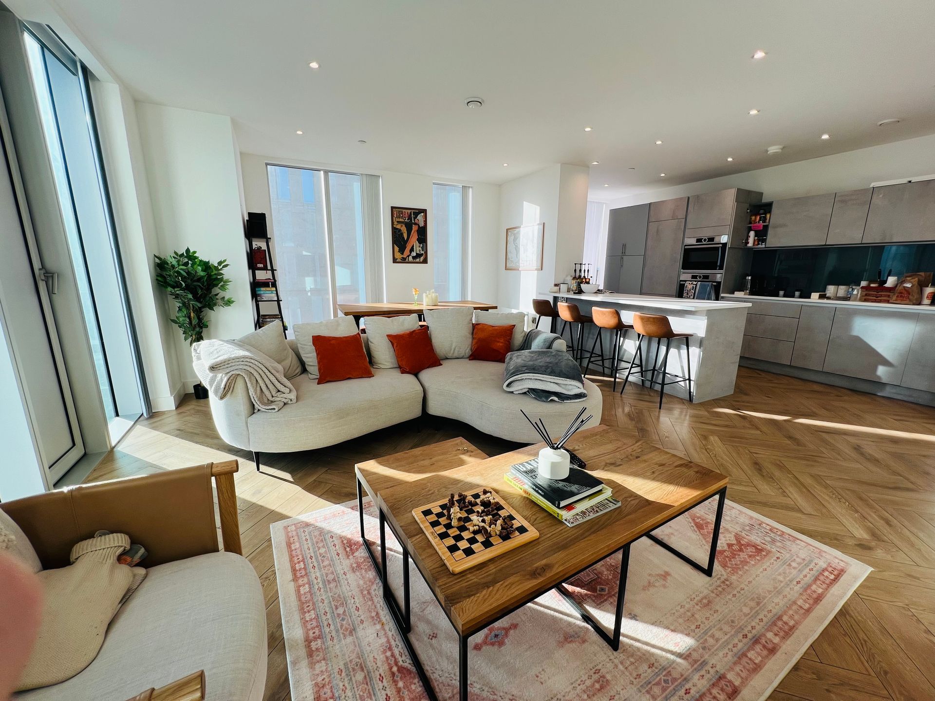 Bright living room with a white sectional sofa, wooden coffee table, and an open kitchen.