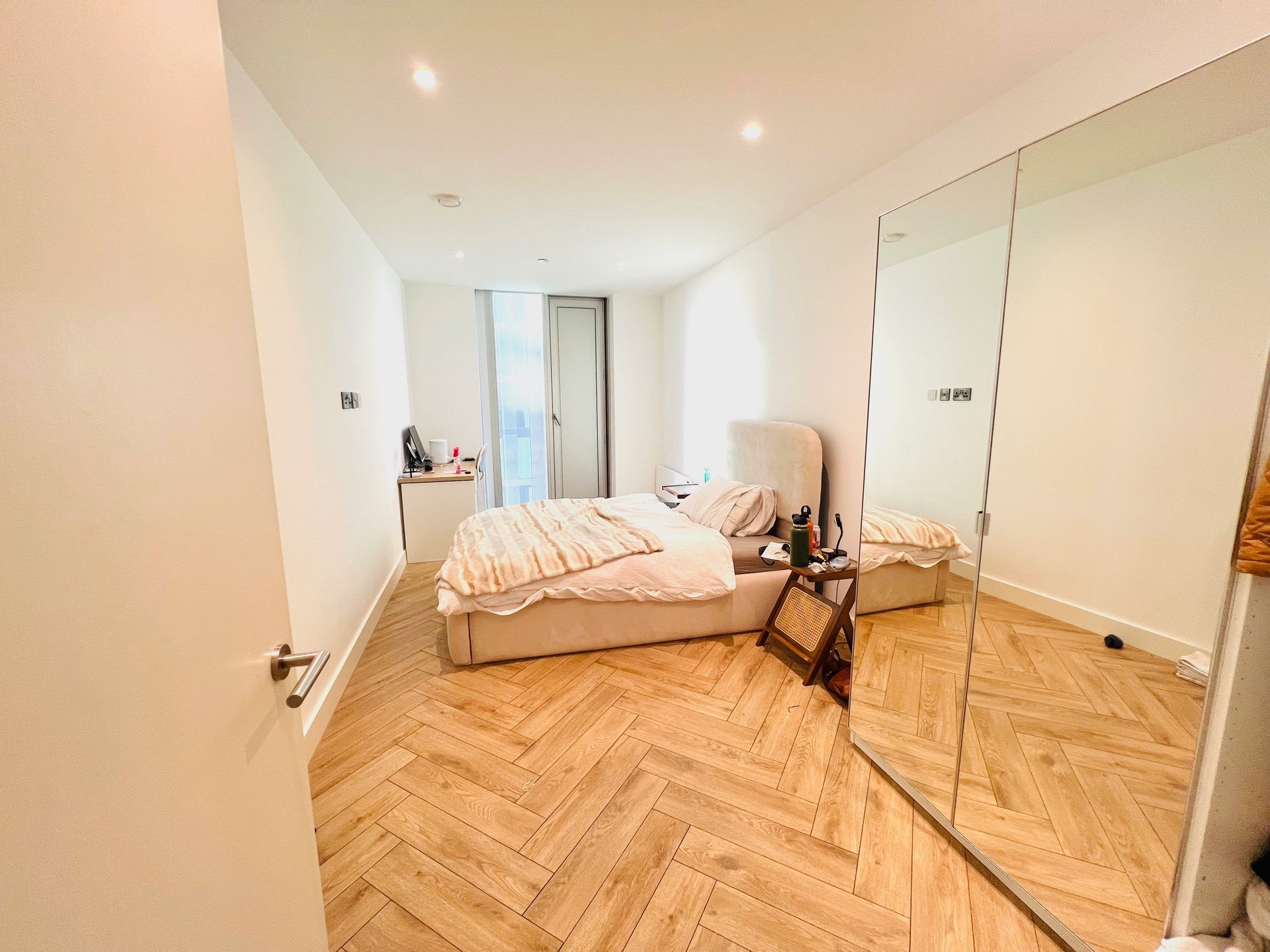 Bedroom with bed, large mirror, and herringbone wood floor.