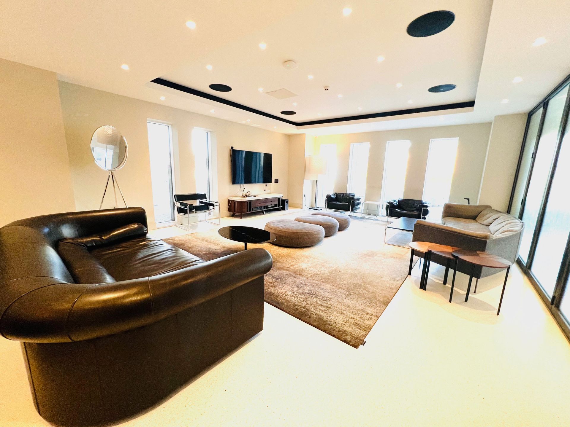Spacious living room with brown leather sofa, rug, and modern furniture. Bright, natural light floods the room.