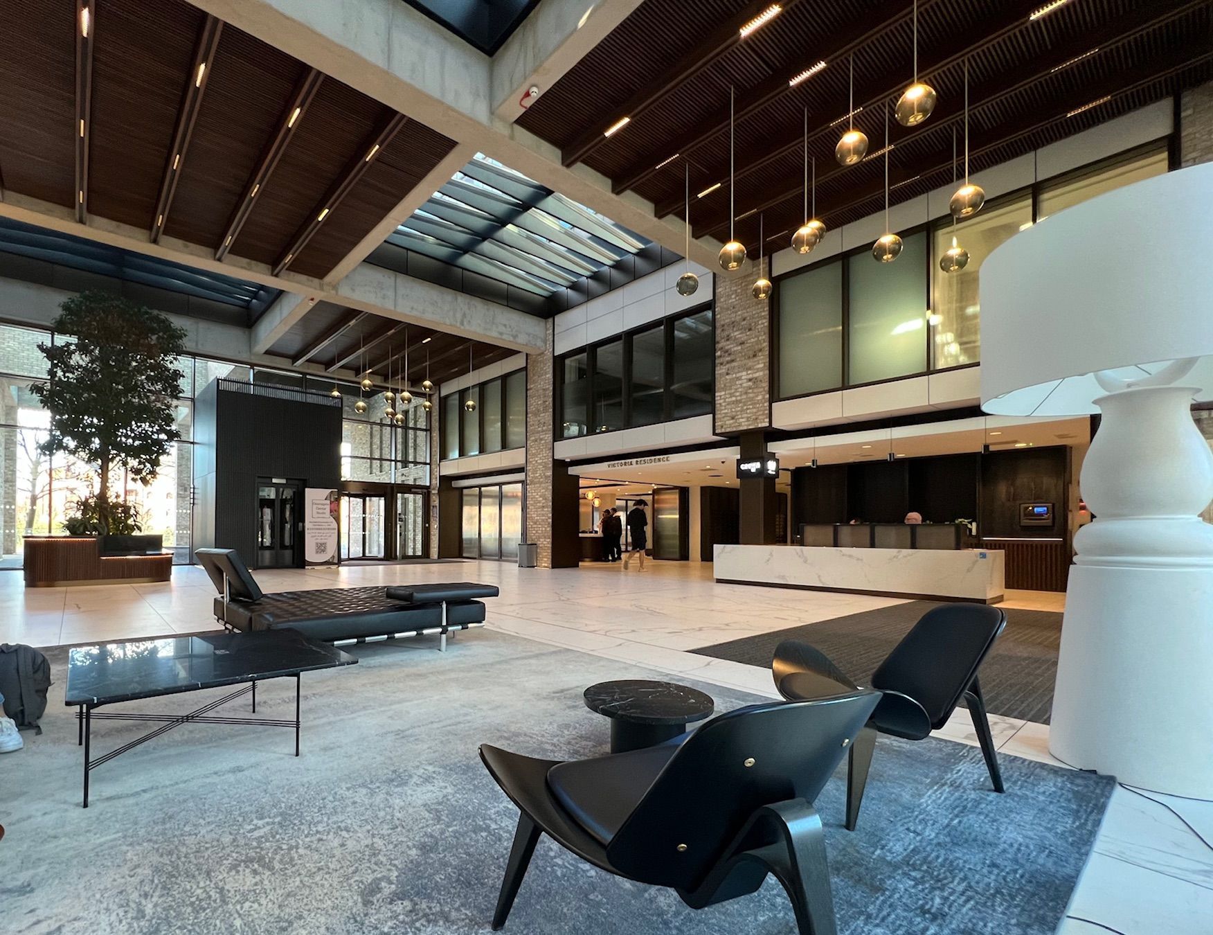 Lobby with seating, reception desk, large windows, and an indoor tree. Brown and white tones.