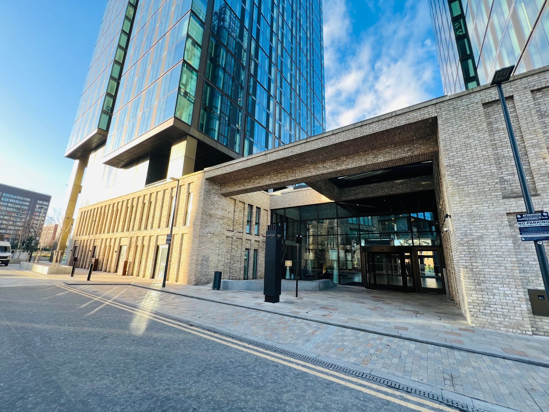 Modern skyscraper entrance with glass facade, stone supports, and street with double yellow lines.