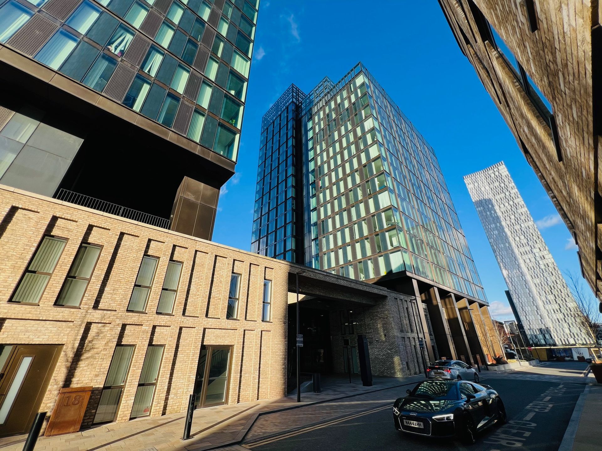 Modern buildings with glass facades and a brick wall. A black car sits on a street.