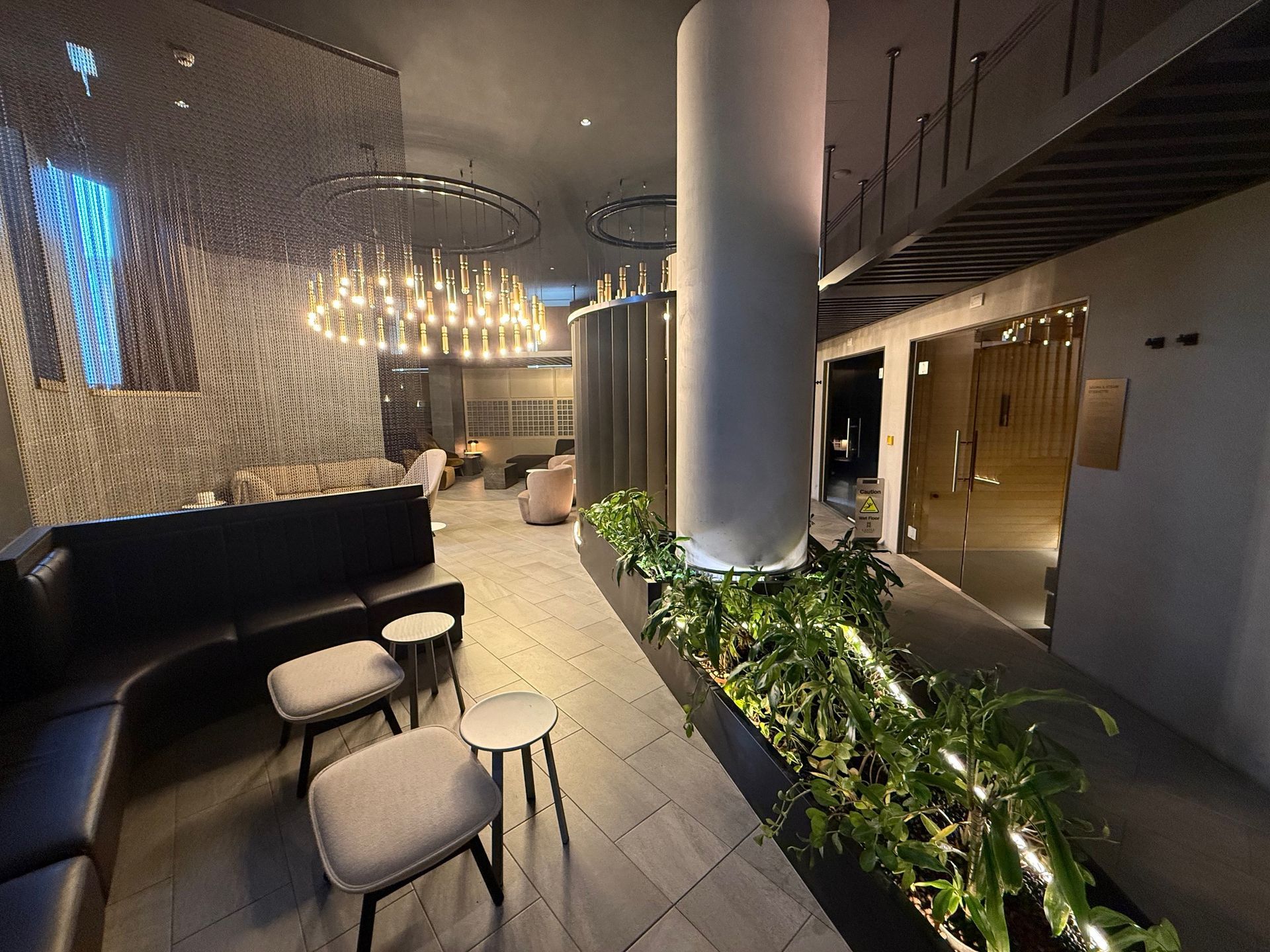 Modern lounge with black seating, small tables, and a central planter with greenery.