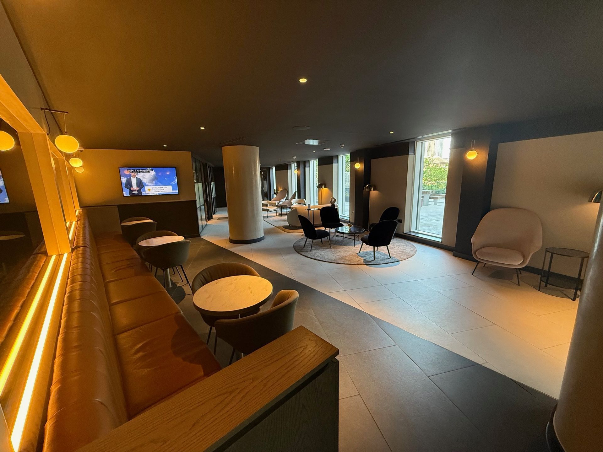 Modern lounge area with seating, small tables, TV, and large windows.