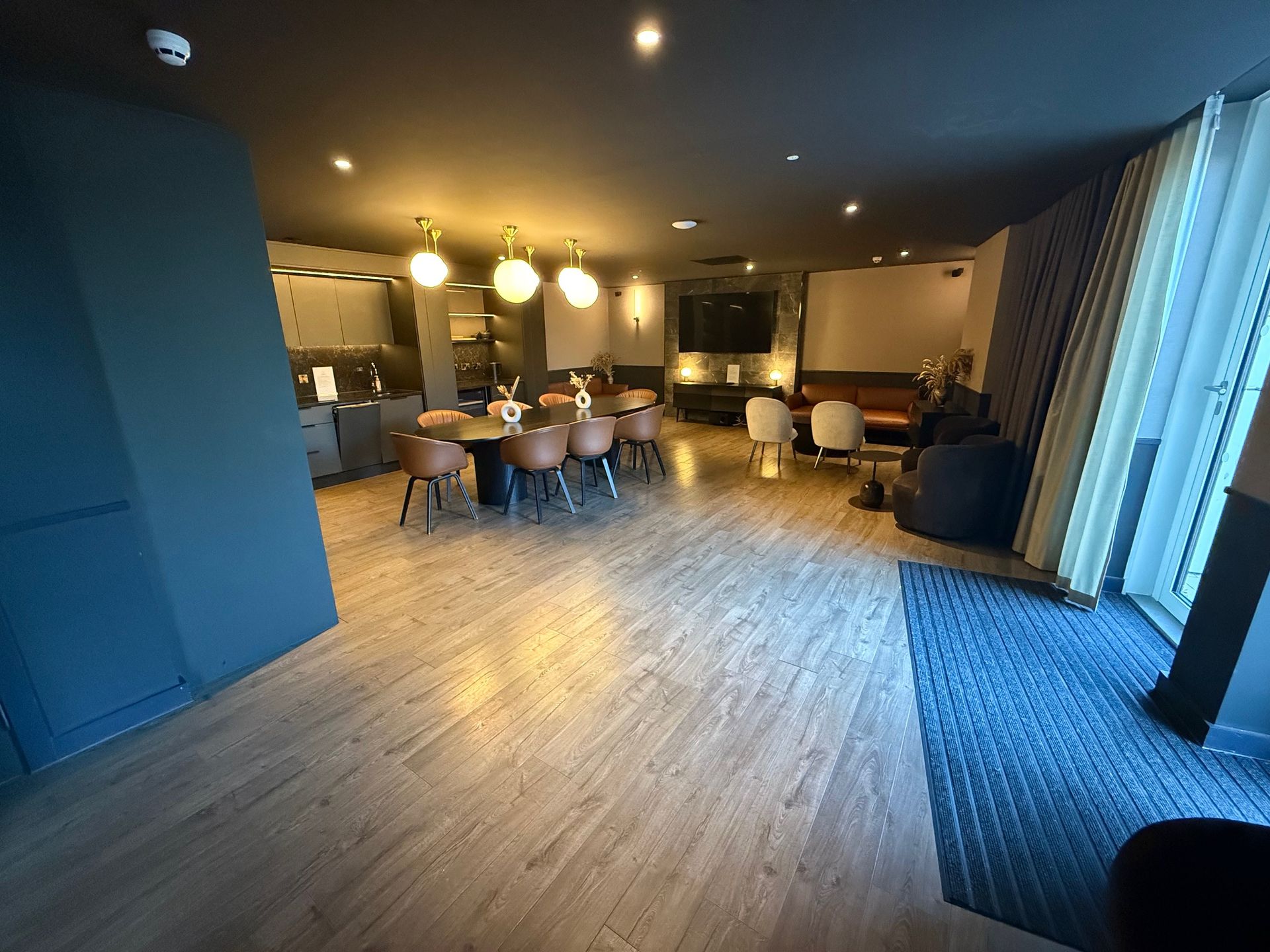Modern lounge area with wooden floors, dining table, chairs, and seating by a window.