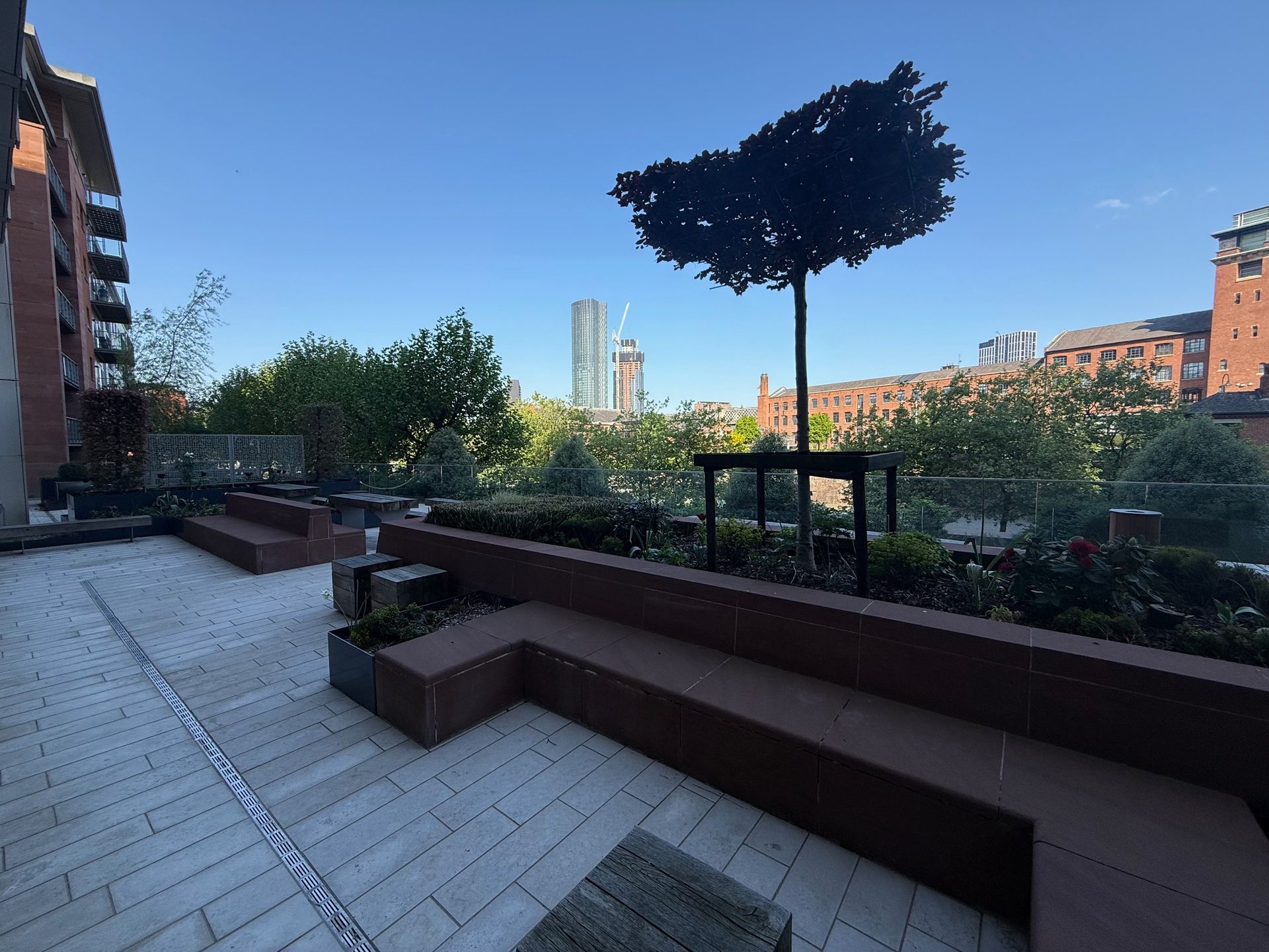 Rooftop patio with seating, trees, and city skyline on a sunny day.