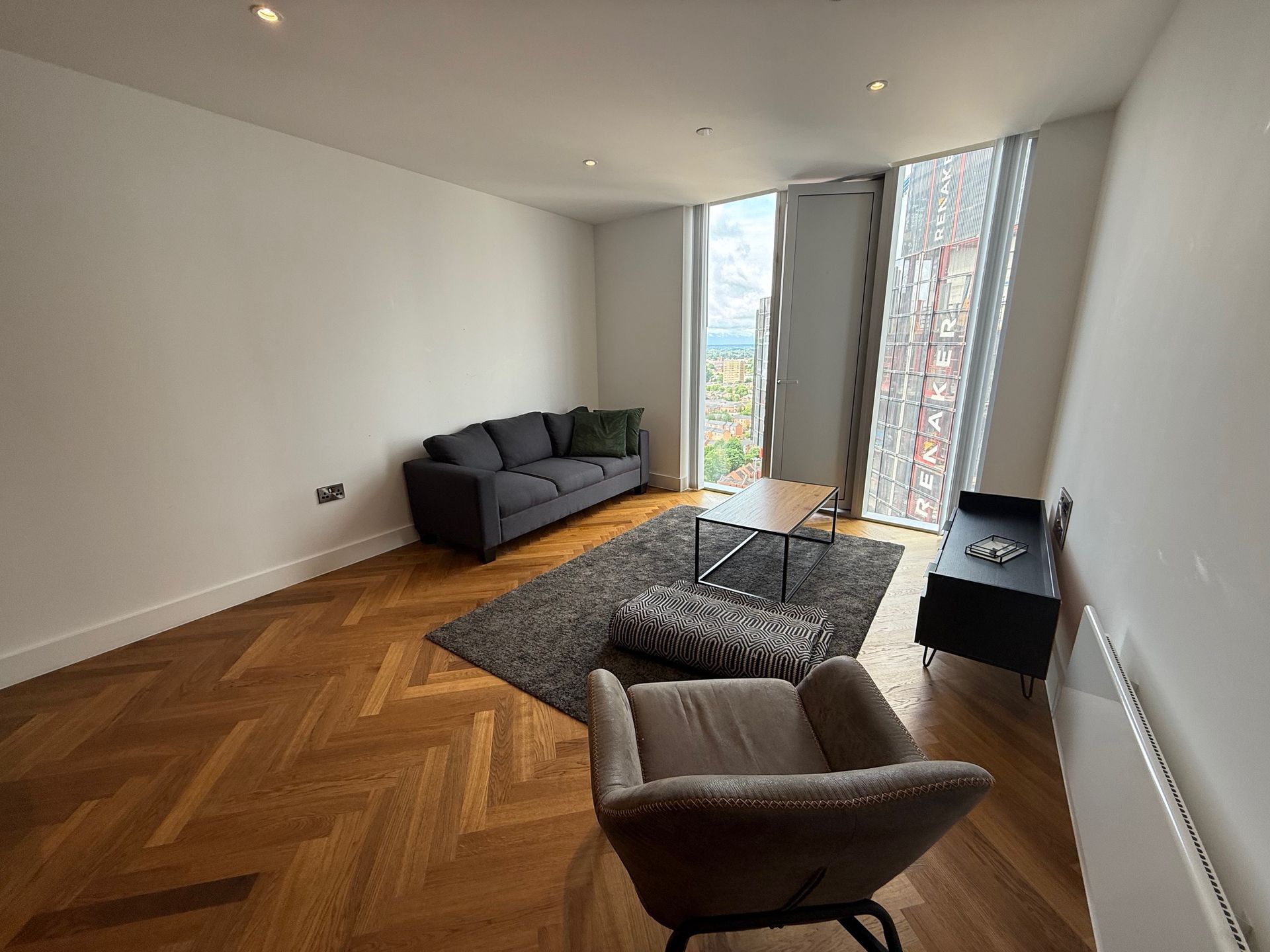 Living room with gray sofa, chair, and rug, hardwood floor, large window, and black media cabinet.