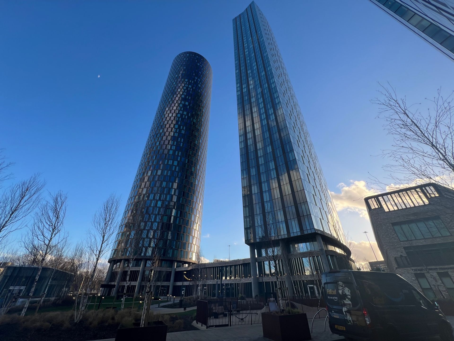 Two tall, modern skyscrapers against a clear blue sky. One is cylindrical, the other rectangular.