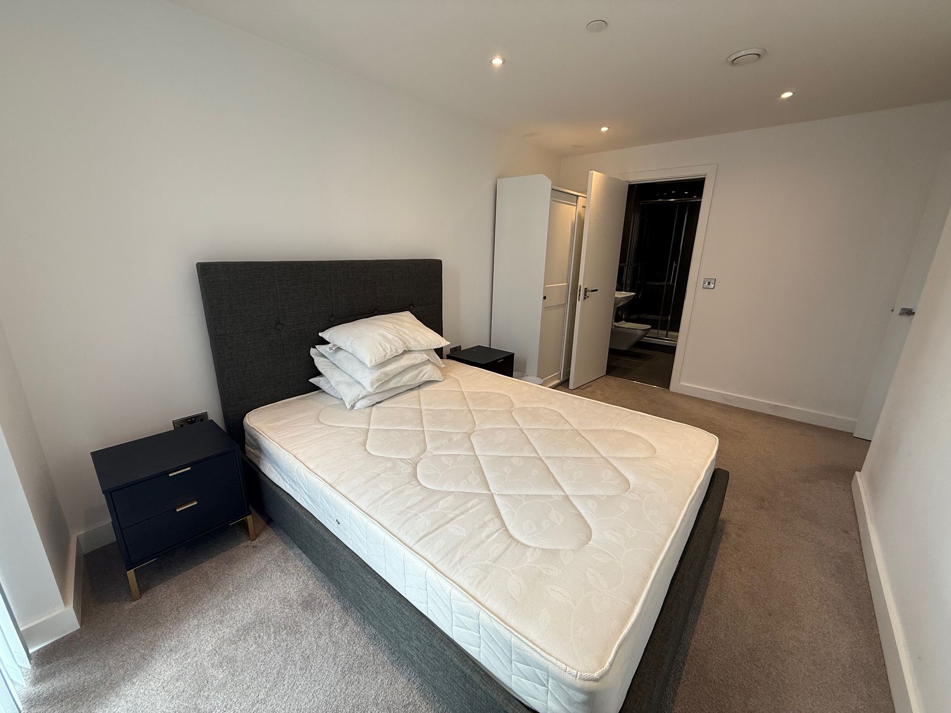 Bedroom with bed, nightstand, wardrobe, and open doorway to a bathroom.
