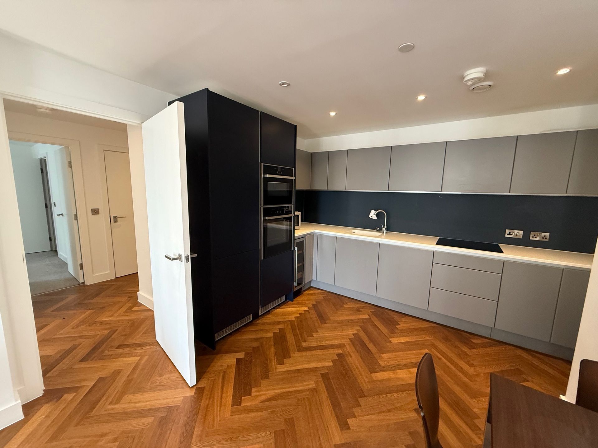 Modern kitchen with wood floors, gray and blue cabinets, and an open doorway to another room.