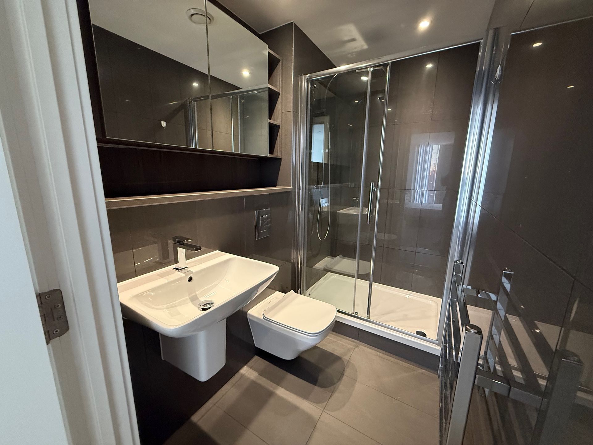 Modern bathroom with gray tiles, shower, sink, and toilet. Mirror and towel rack.