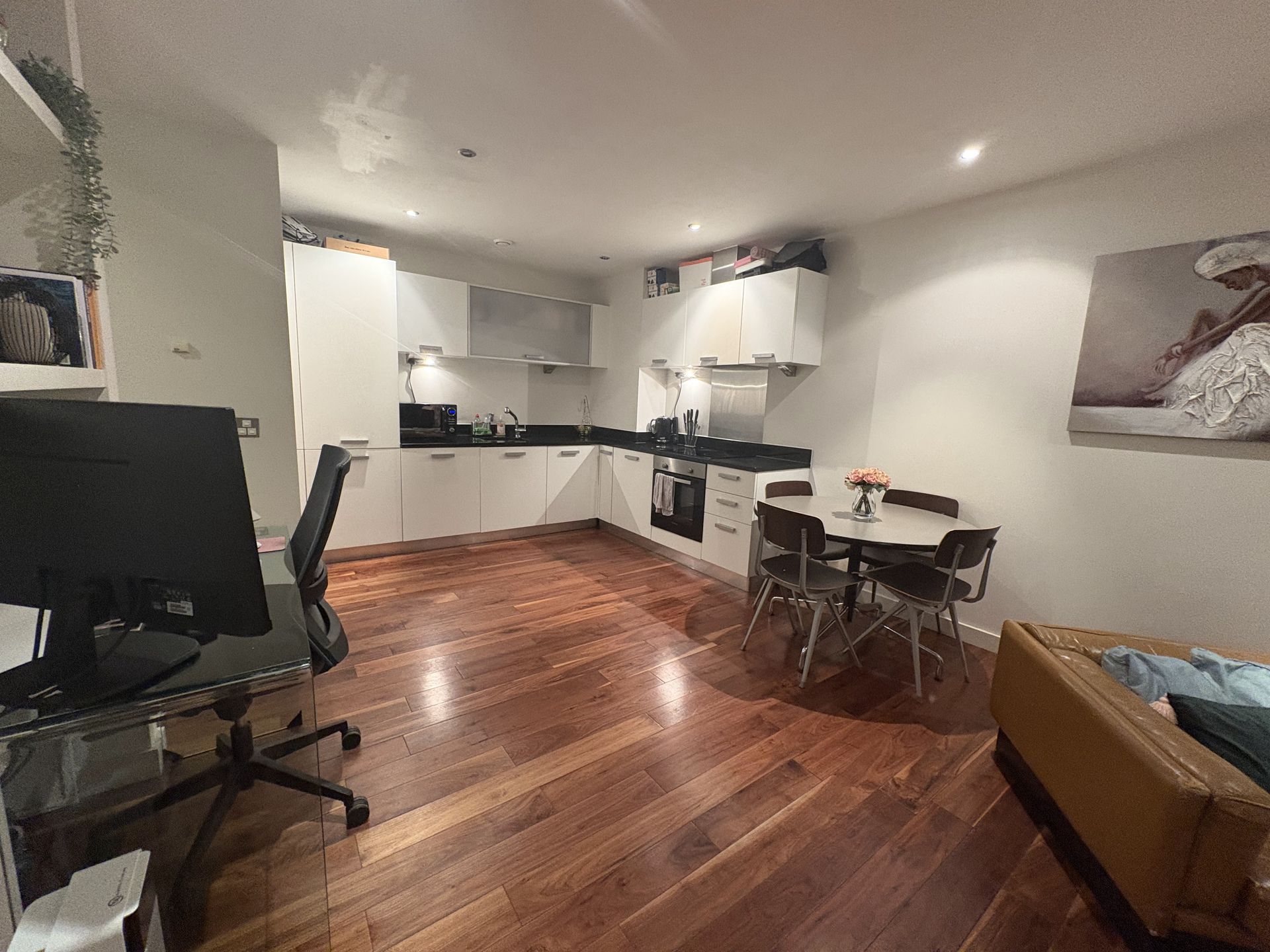 Wooden-floored kitchen and dining area with cabinets, appliances, table and chairs. A computer desk is in the foreground.