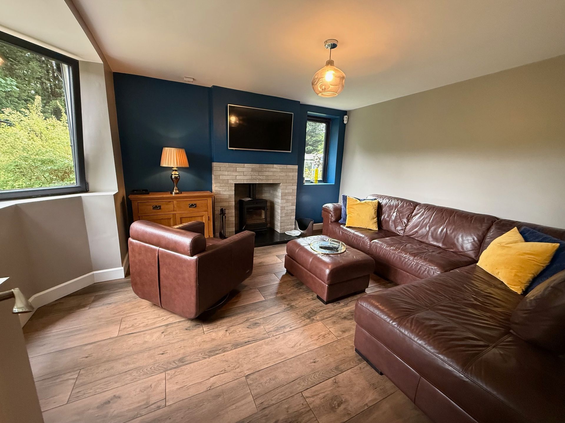 Living room with brown leather sofa, chair, ottoman, fireplace, TV, and wood-look flooring.
