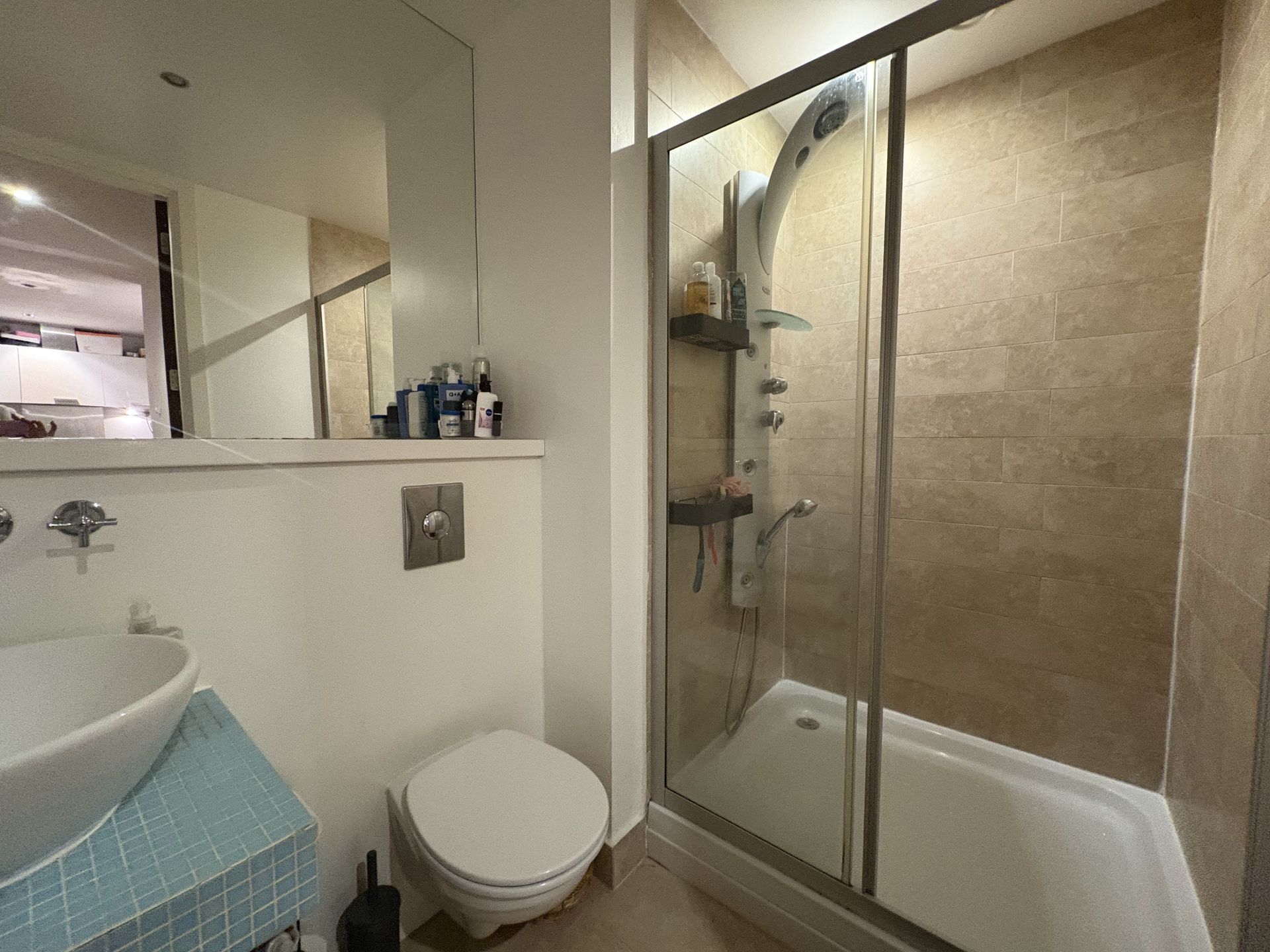 Bathroom with shower, toilet, sink, and mirror. Beige tile walls.