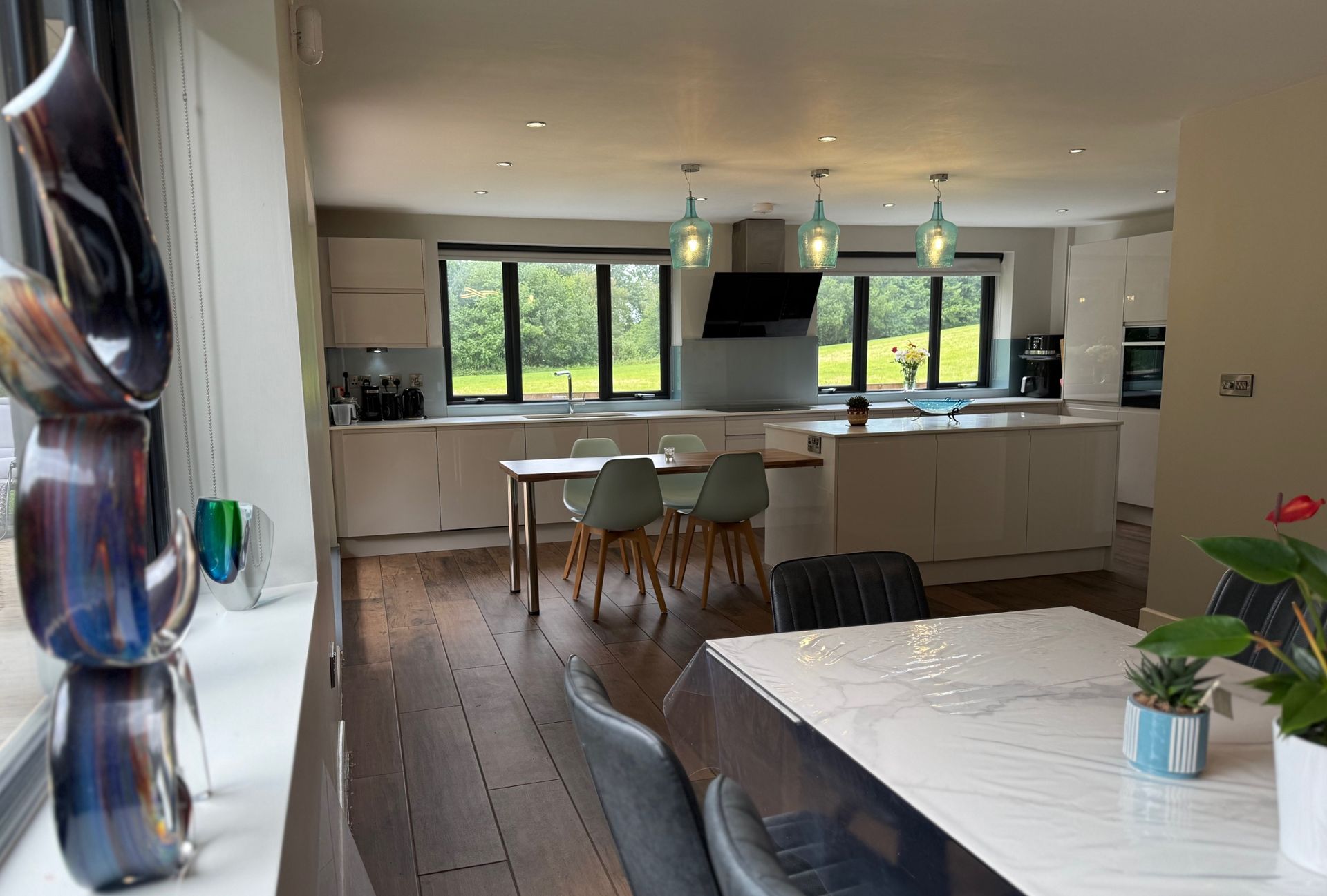 Modern kitchen with light cabinets, wood floors, and view to outdoors. Dining area with table and chairs.