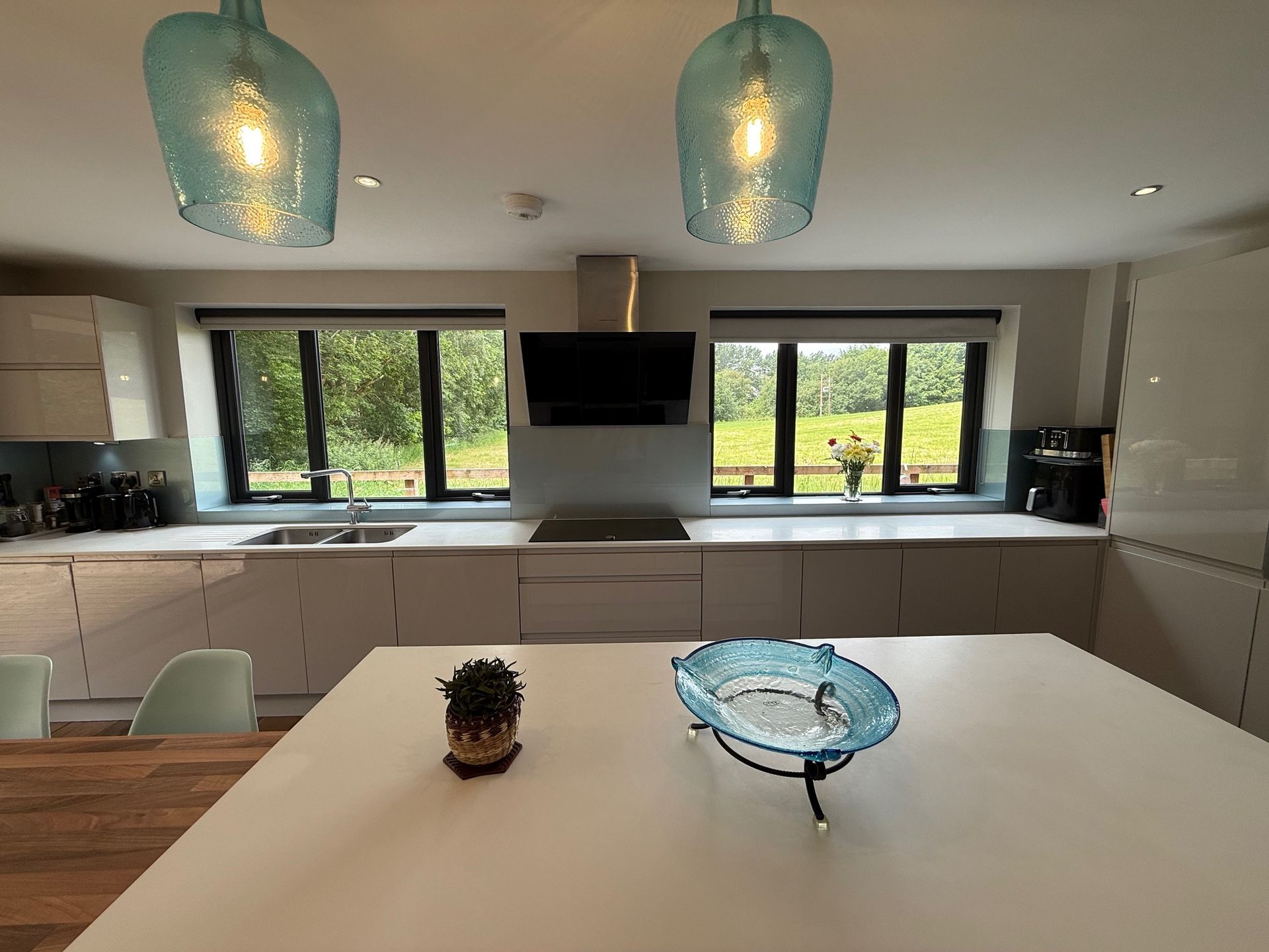 Modern kitchen with a white island, two blue glass pendant lights, and windows overlooking greenery.