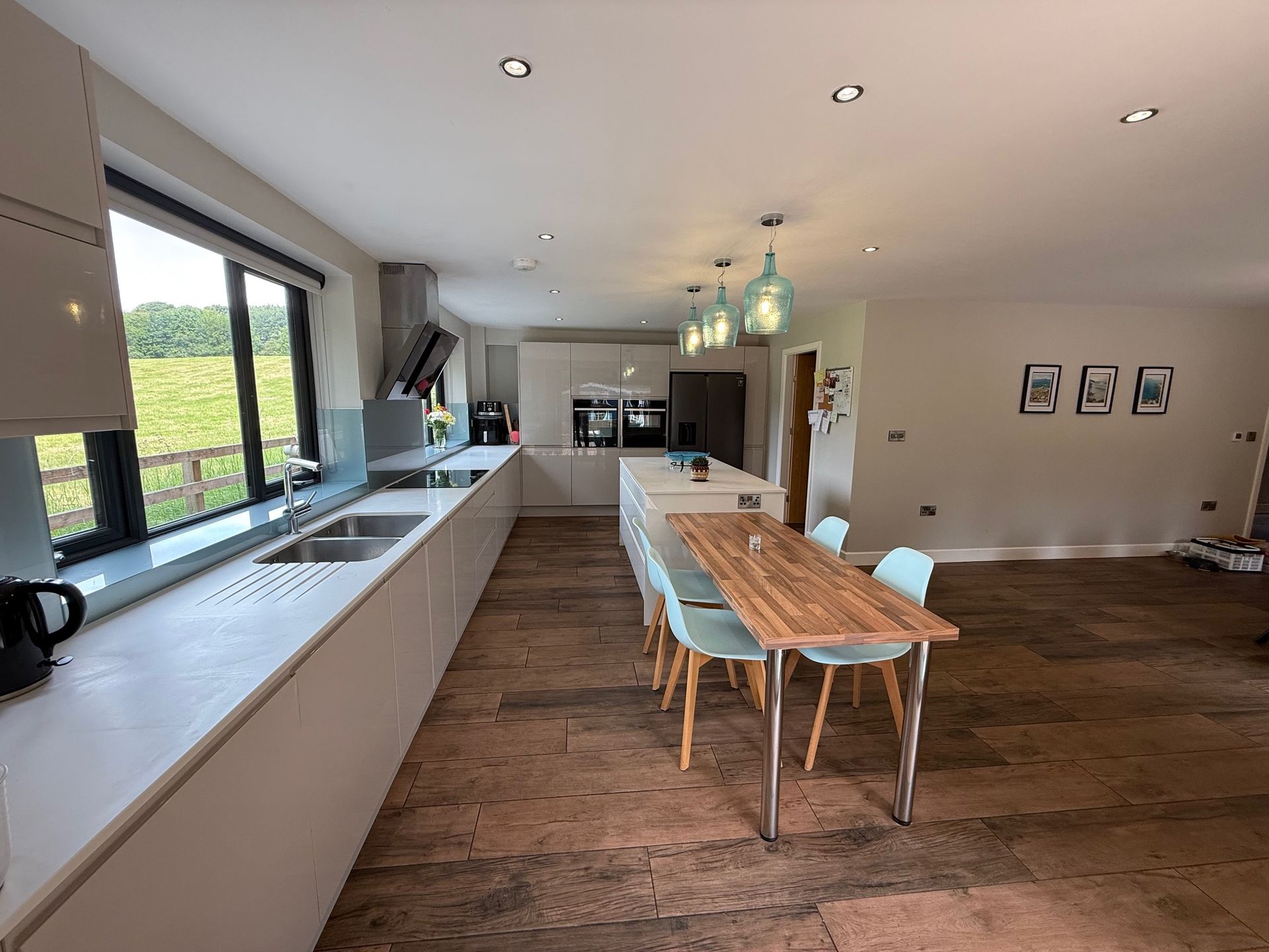 Modern kitchen with long island and dining table; light cabinets, stone floor, large windows.