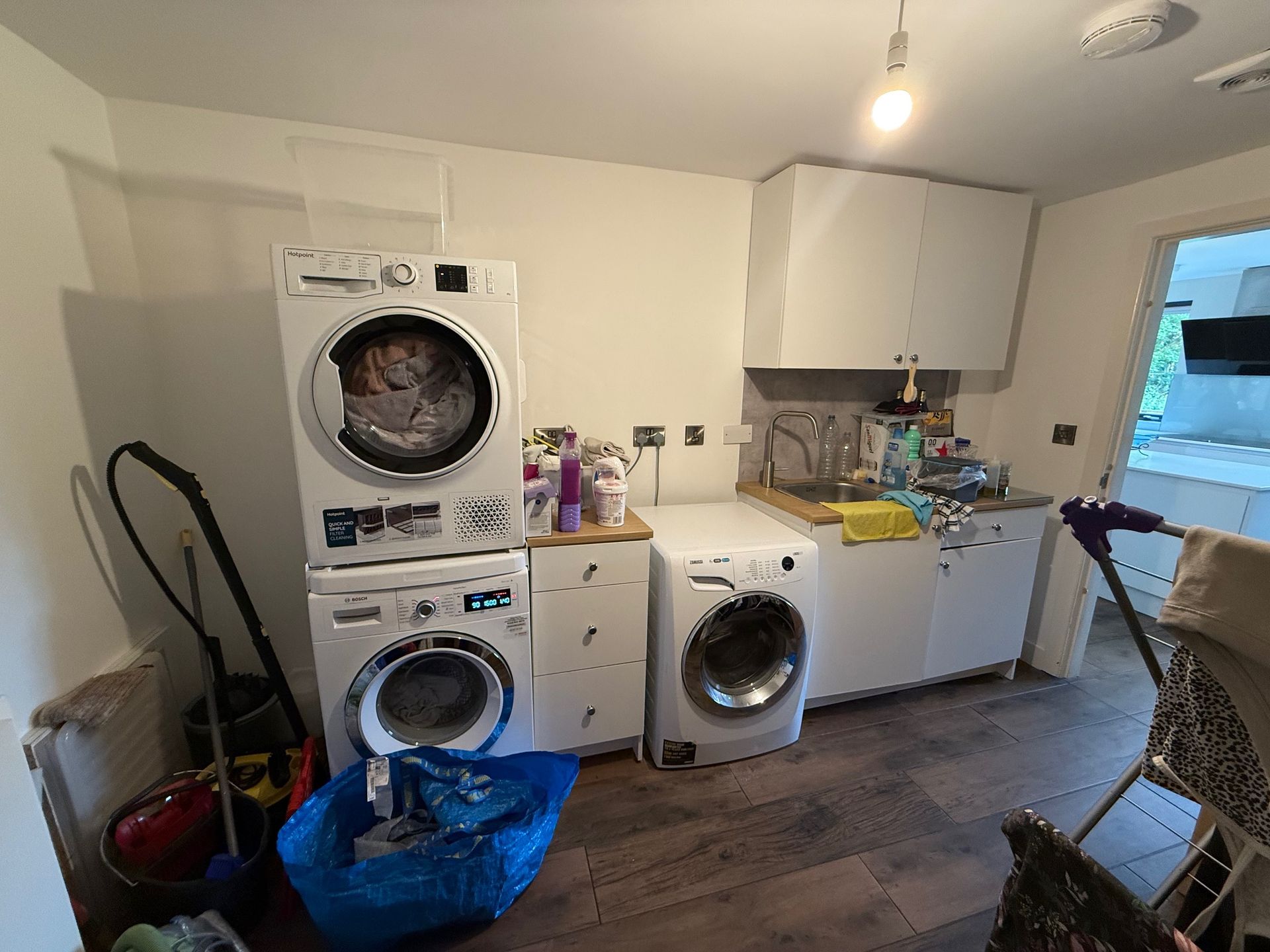Laundry room with stacked washer and dryer, additional washer, cabinets, sink, and clutter.