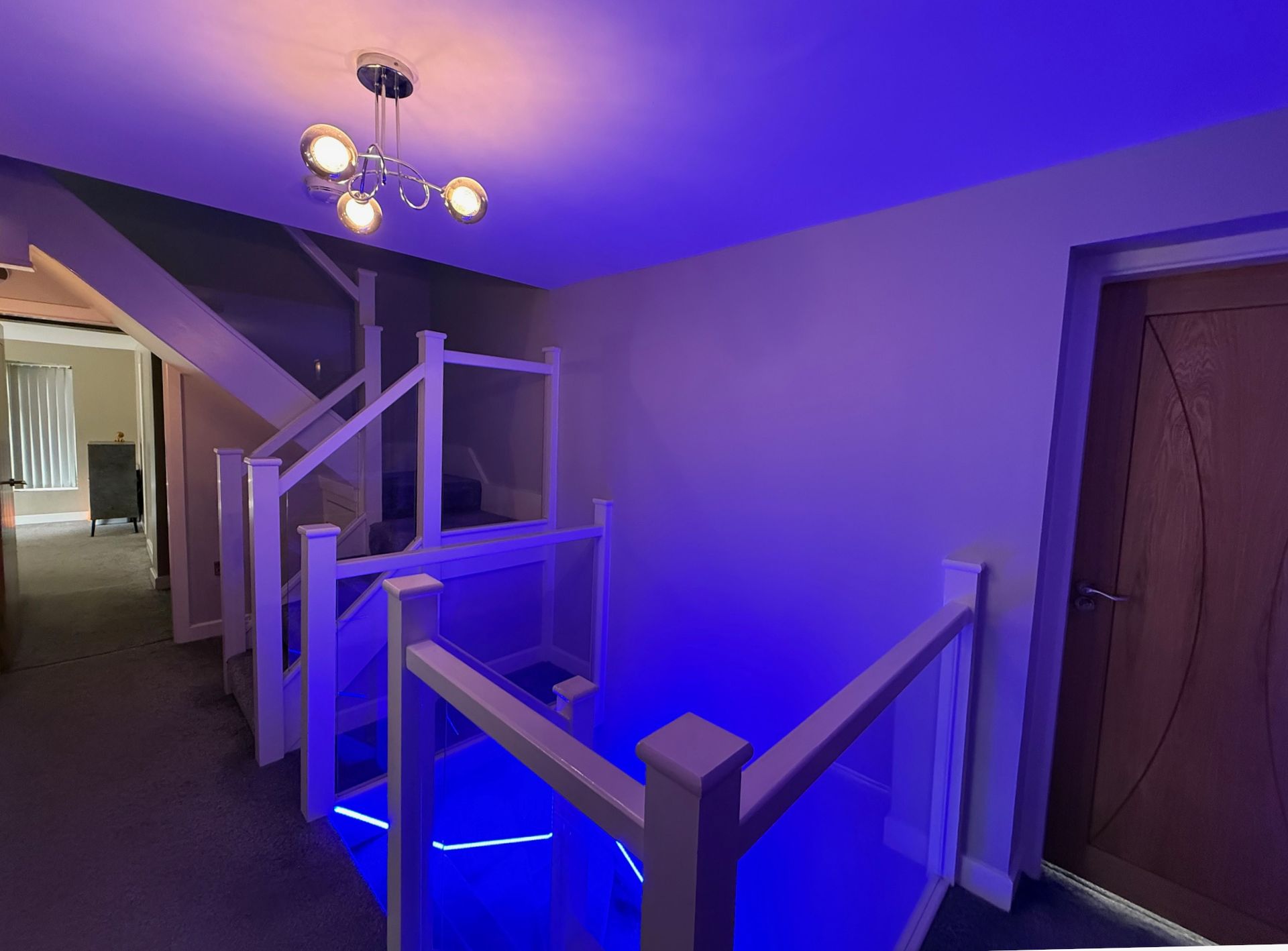 Stairwell with glass panels, white railing, and blue LED lighting. Modern design.