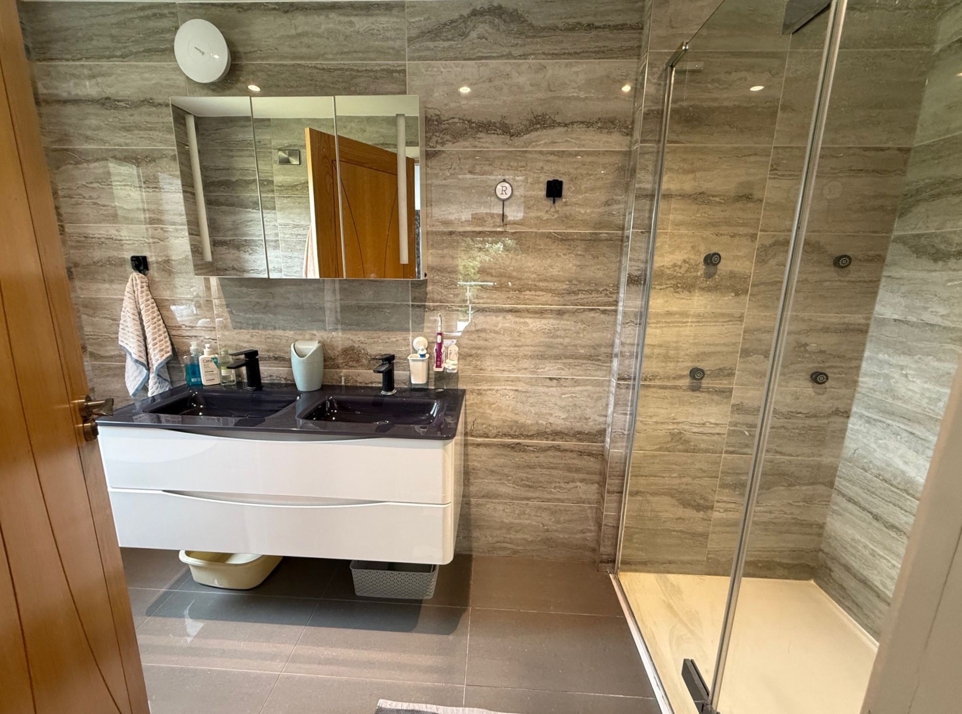 Modern bathroom with gray and wood-tone tiles, a floating vanity, and a glass shower.
