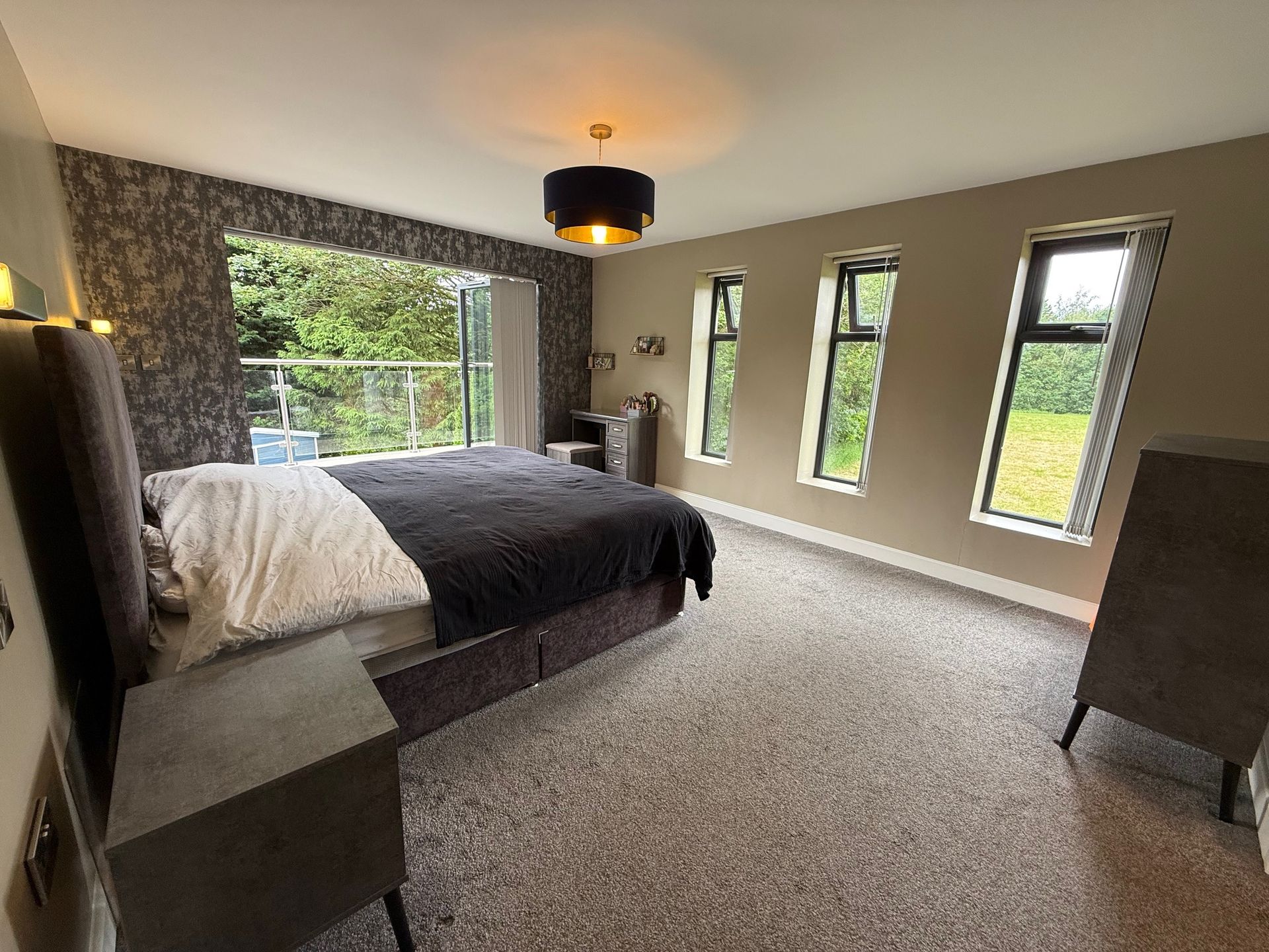 Bedroom with bed, windows, and dark furniture. Features floral wallpaper and a large window with greenery view.