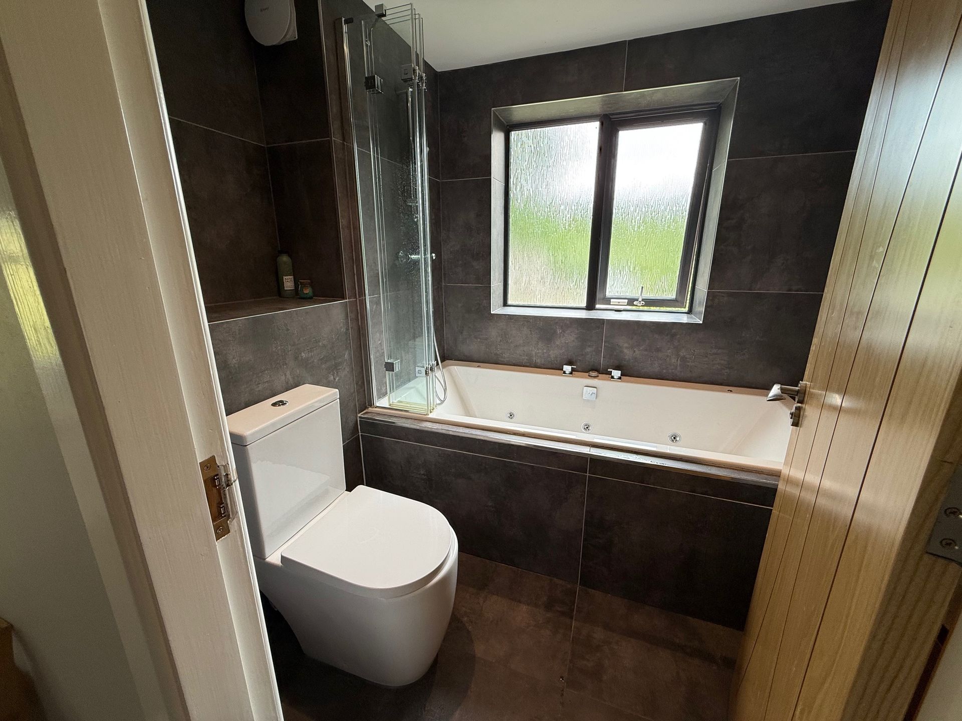Modern bathroom with a toilet, bathtub, window, and dark gray tiles.