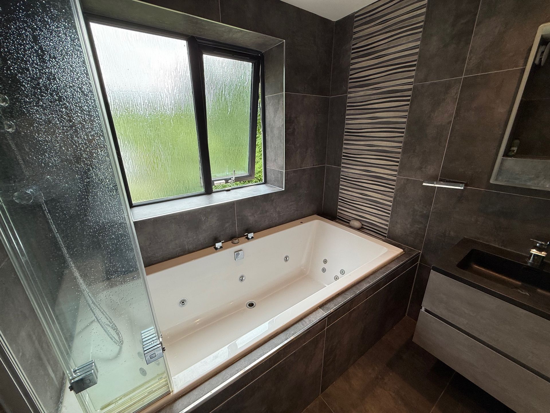 Bathroom with a jacuzzi tub, window, and modern tile.