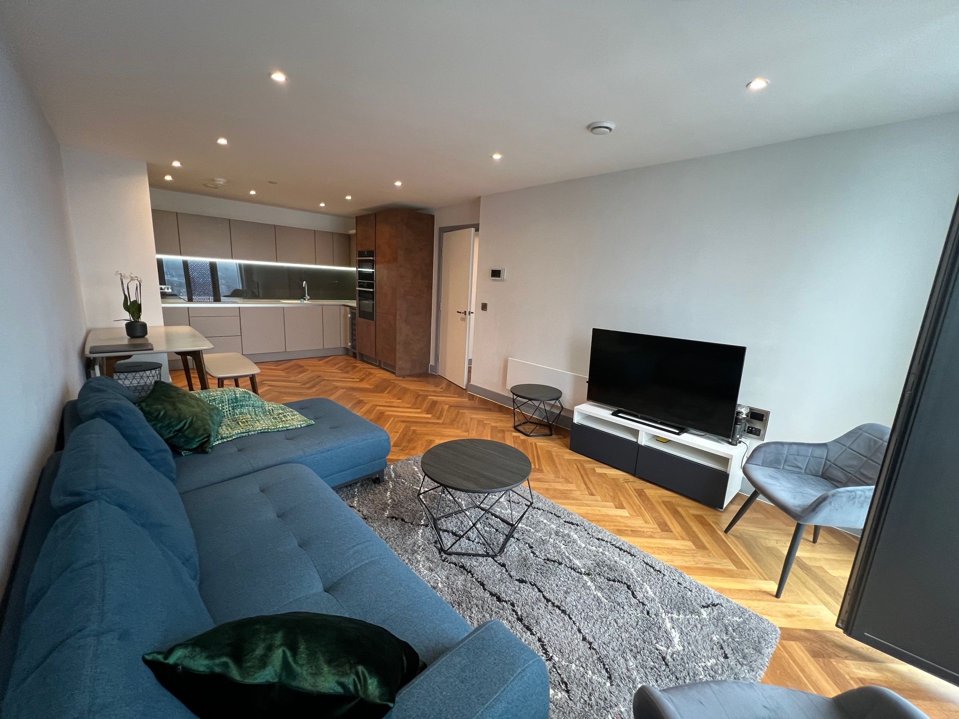 Blue sectional sofa in modern living room with TV, rug, and kitchen in the background.