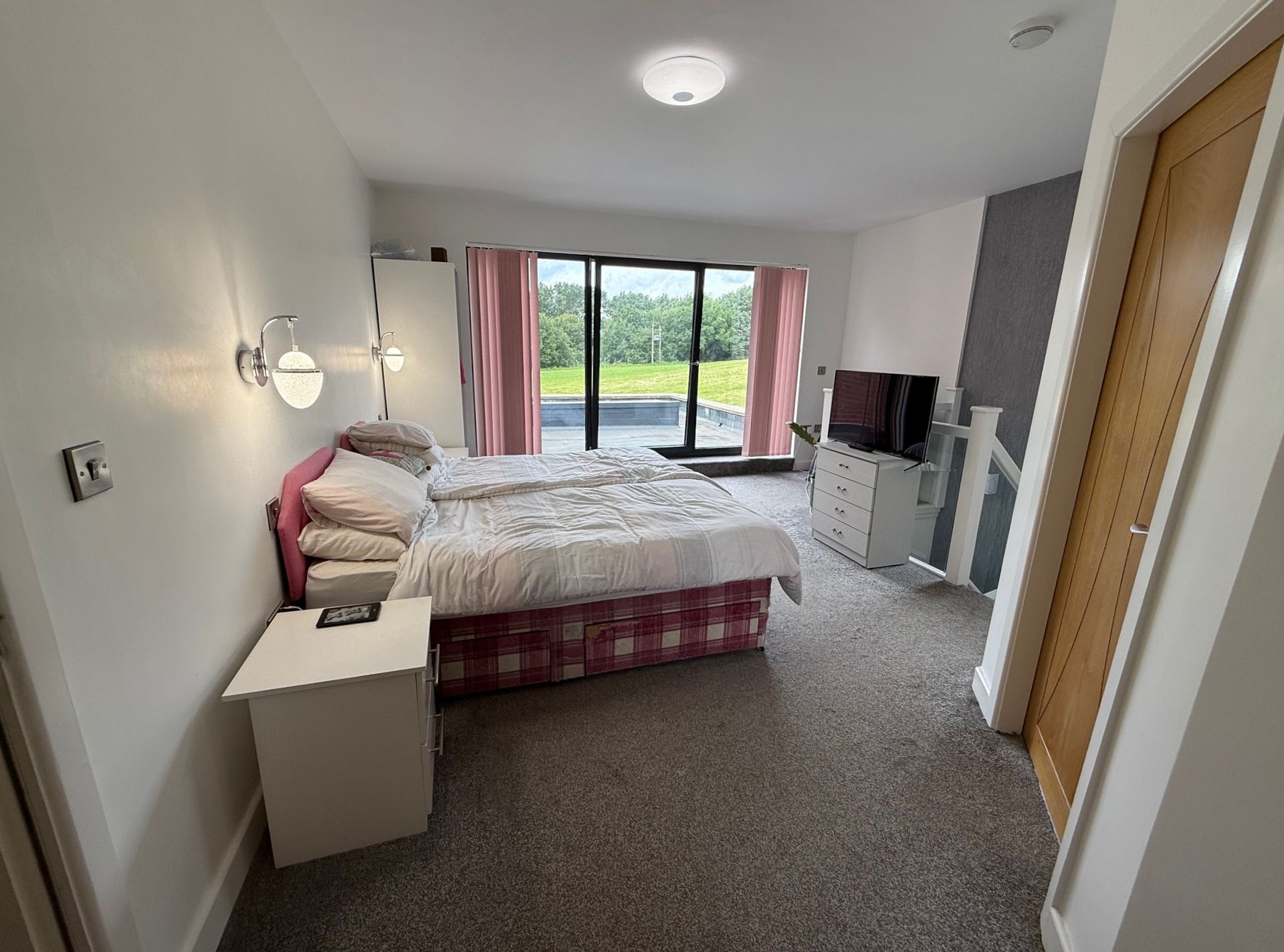 Bedroom with bed, closet, TV, and large glass doors leading to a green space.