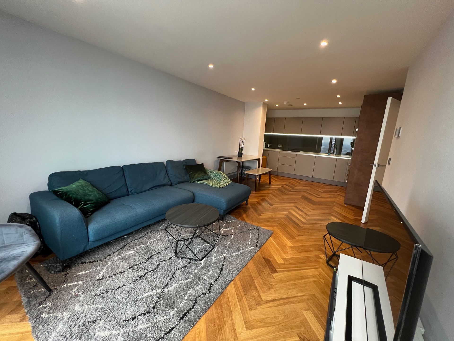 Living room with blue sectional sofa, area rug, coffee tables, and parquet flooring.