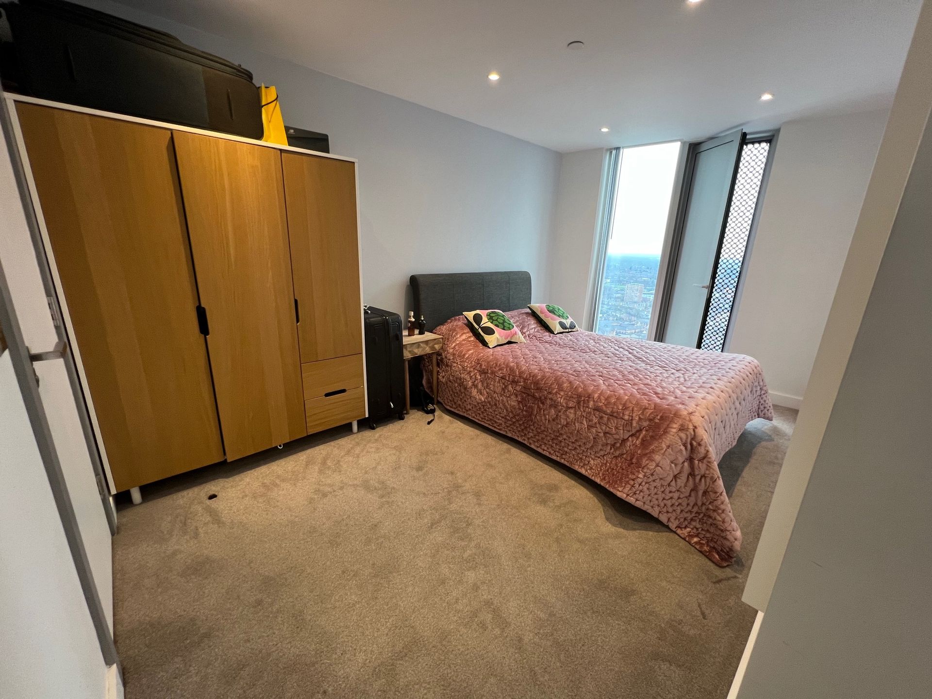 Bedroom with a bed, a wardrobe, and a large window. The bed has a pink bedspread.